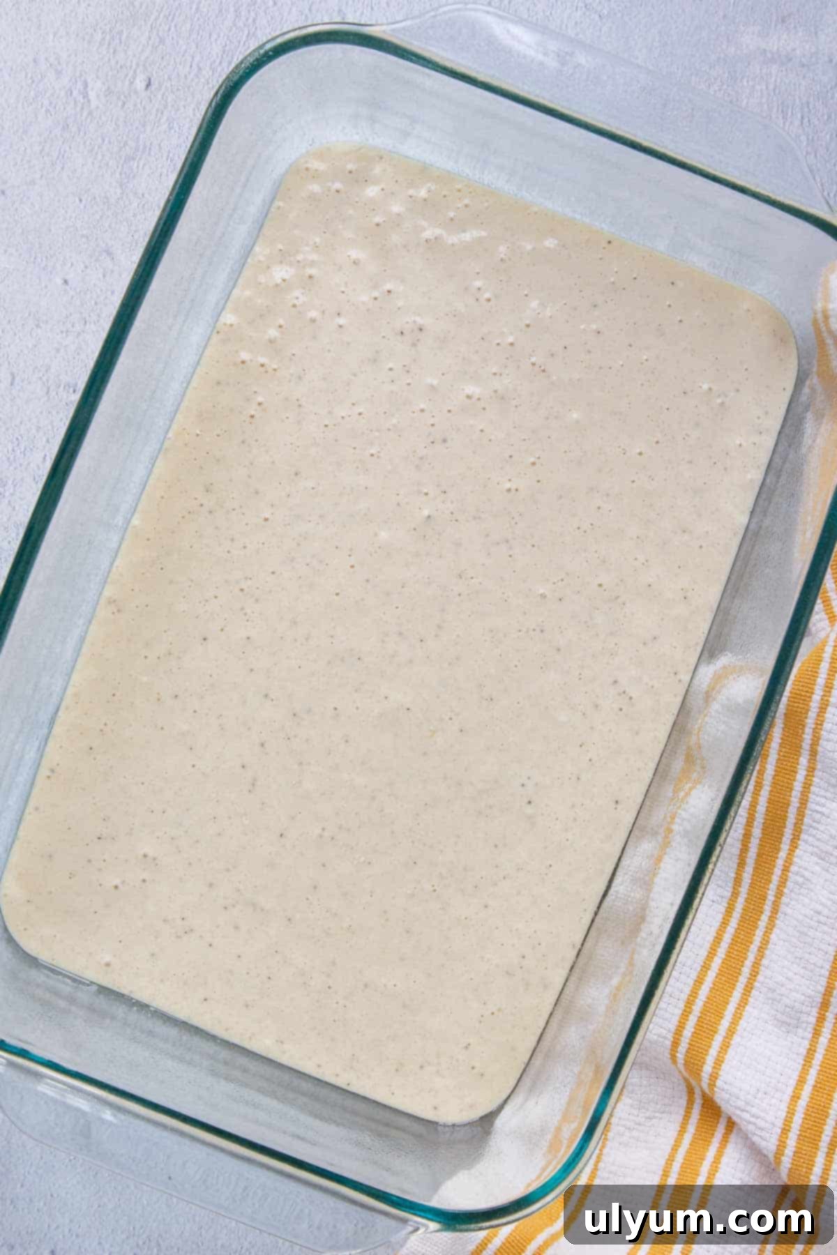 The smooth Bisquick mixture poured evenly into the prepared 9x13-inch baking dish, forming the base layer of the casserole.