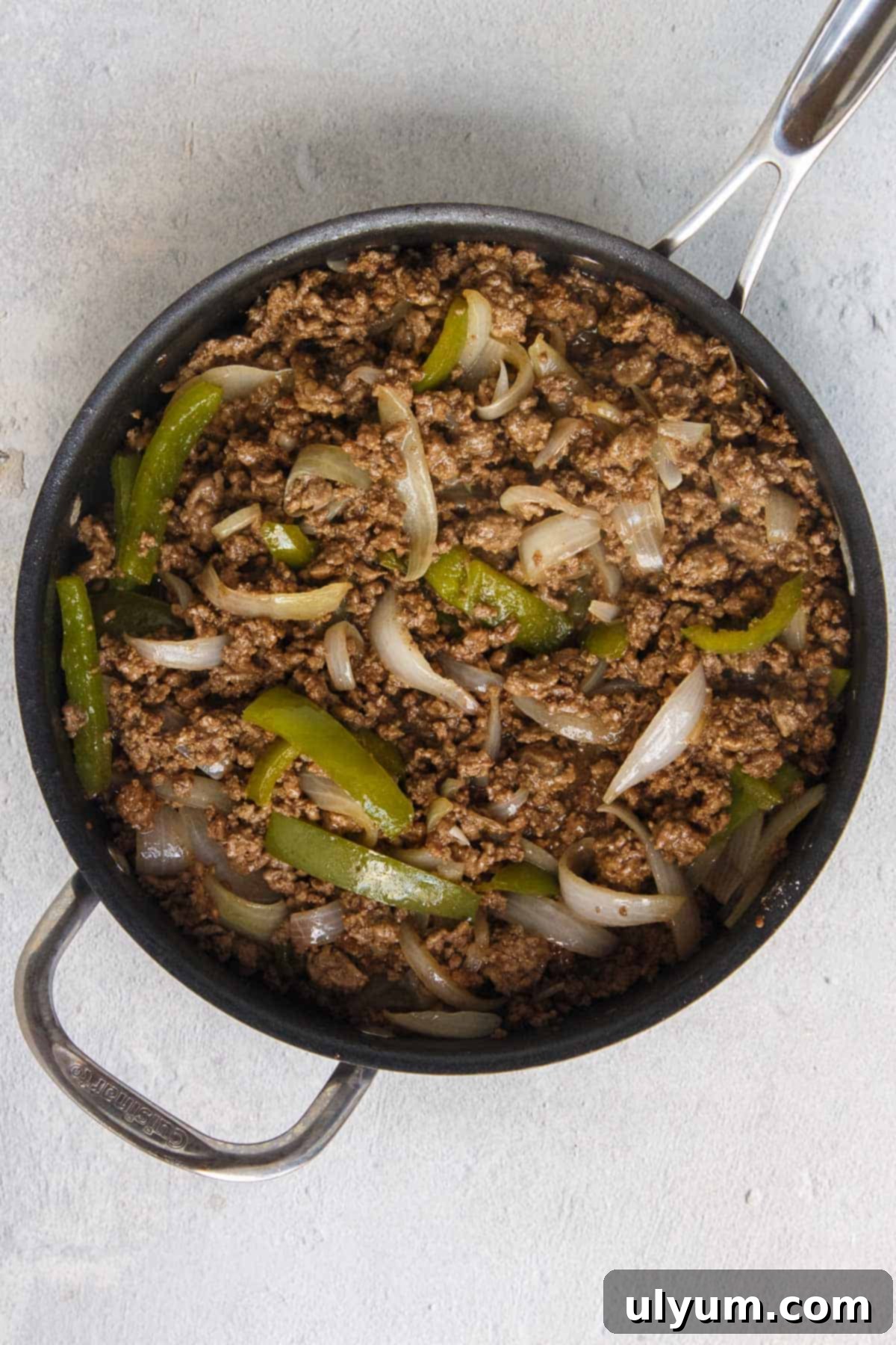 Sautéed ground beef, sweet onions, and green bell peppers in a skillet, with excess grease drained, forming the flavorful base of the casserole.