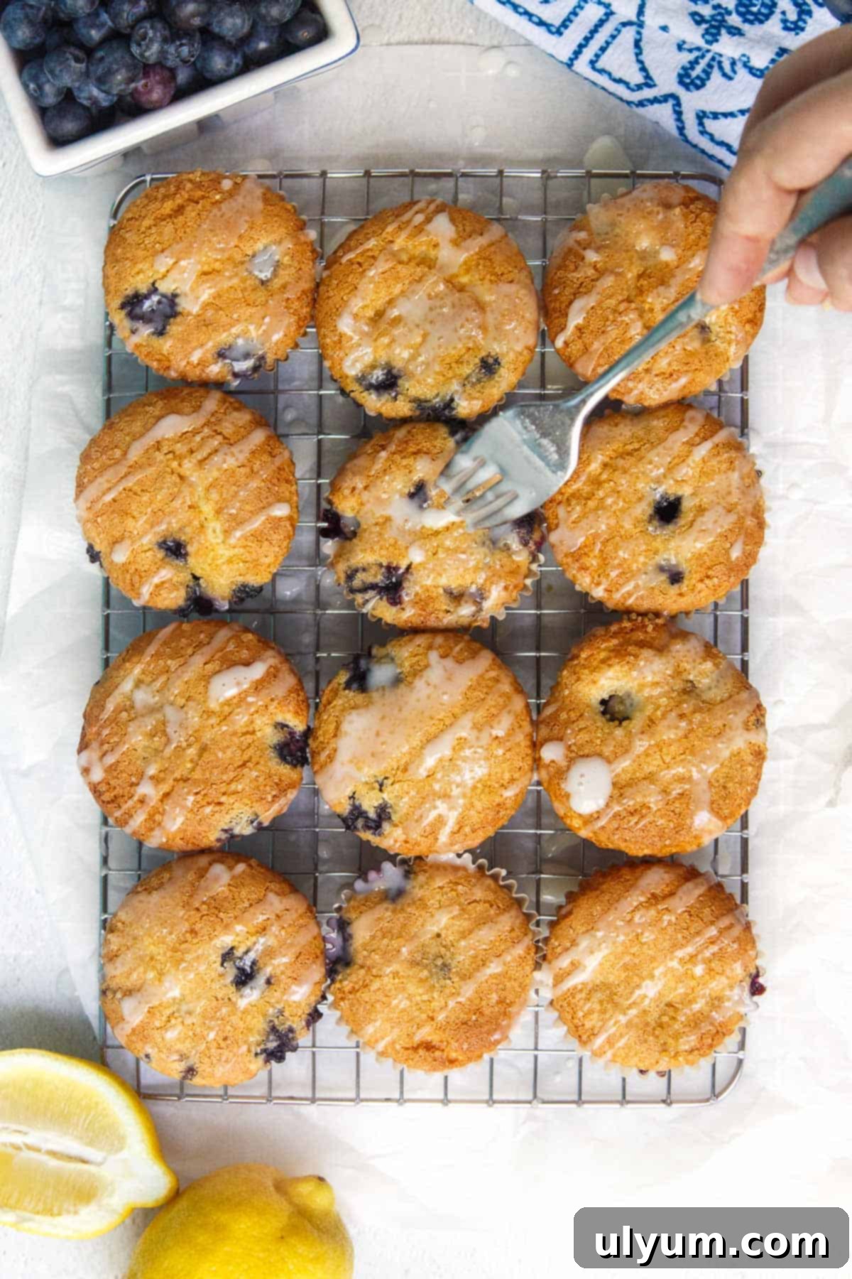 Drizzling homemade lemon powdered sugar glaze over completely cooled cake mix blueberry muffins using a fork.
