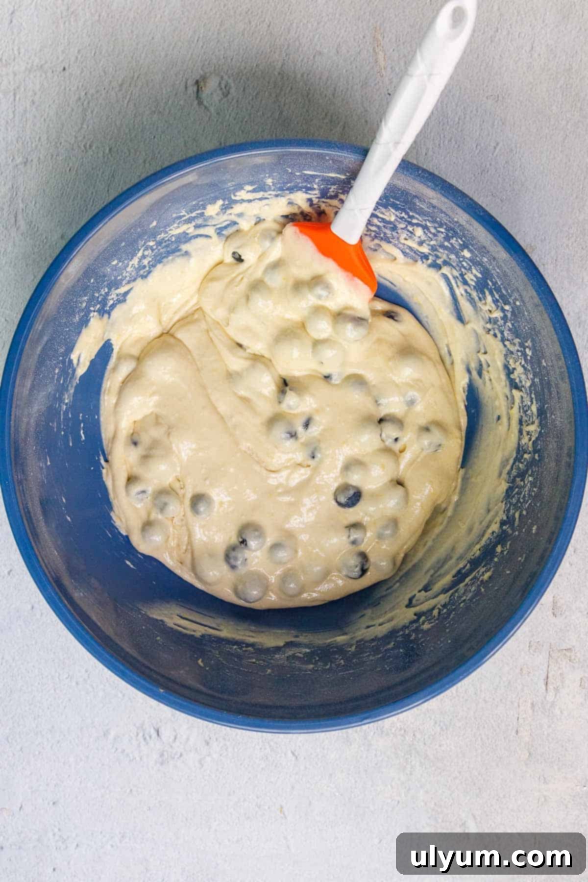 Cake mix blueberry muffin batter in a large mixing bowl with fresh blueberries gently folded in using a silicone spatula.