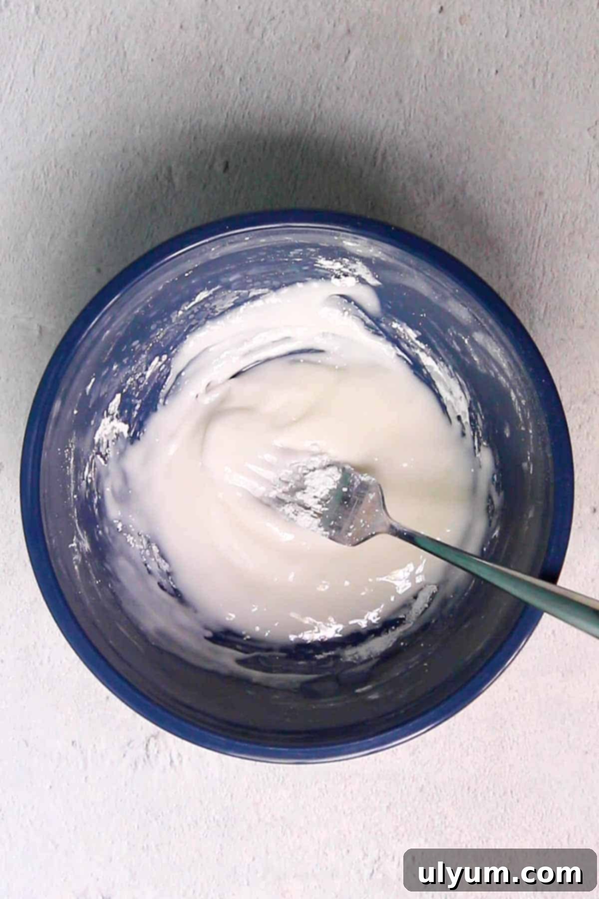 Powdered sugar and fresh lemon juice being stirred together in a small mixing bowl to create the lemon glaze.