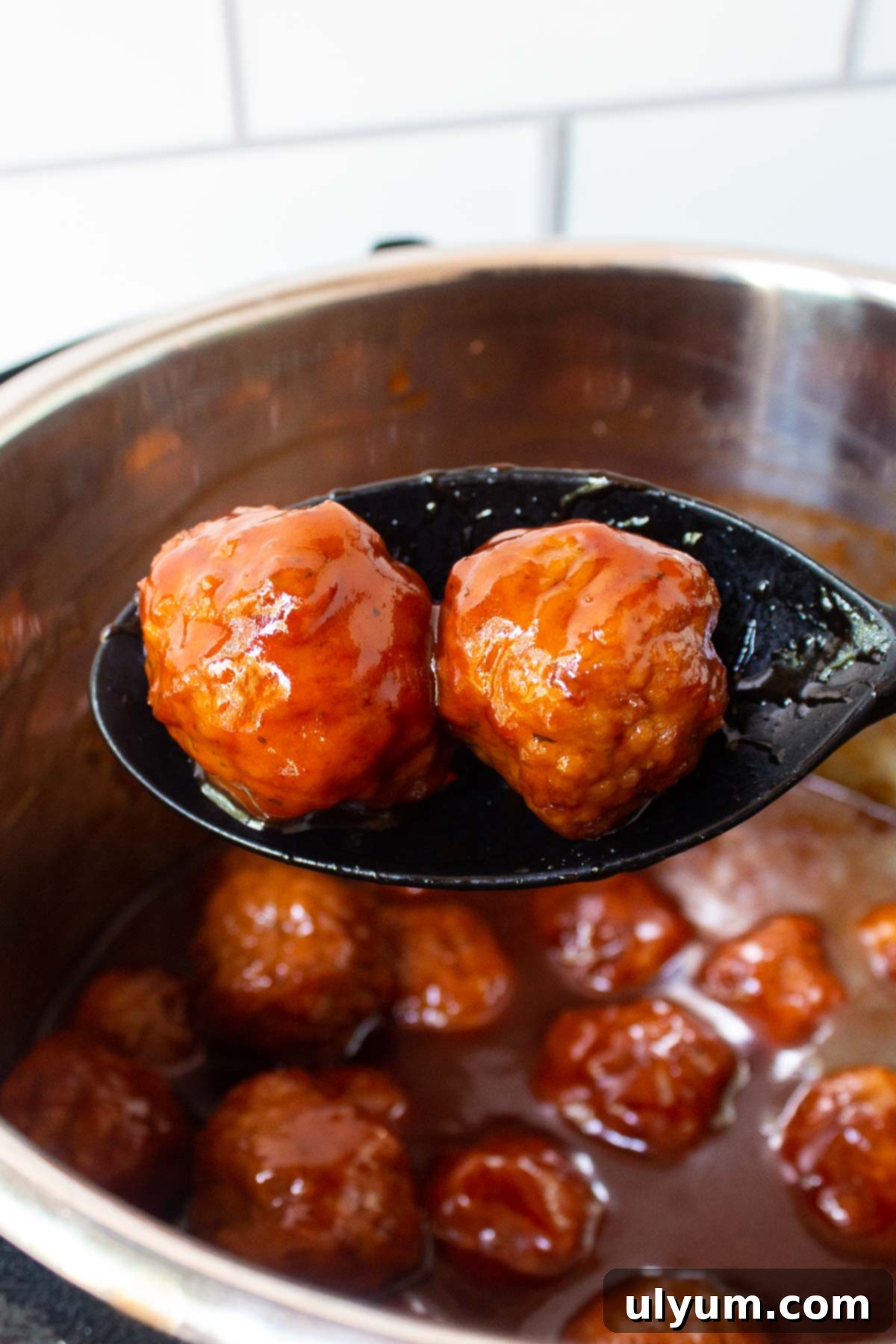 Two Instant Pot Grape Jelly Meatballs on a silicone serving spoon, illustrating the saucy consistency.