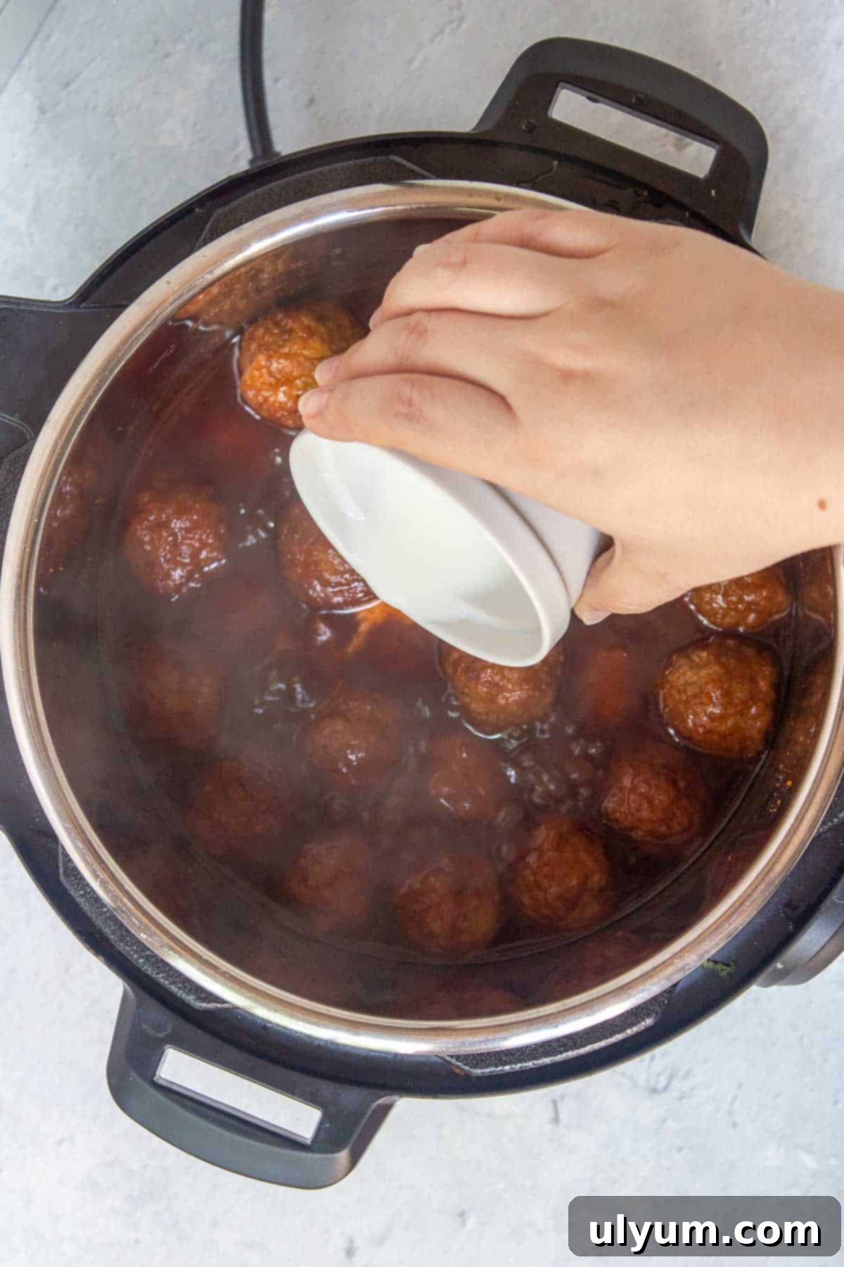 Pouring a cornstarch slurry over the meatballs in the Instant Pot to thicken the sauce.