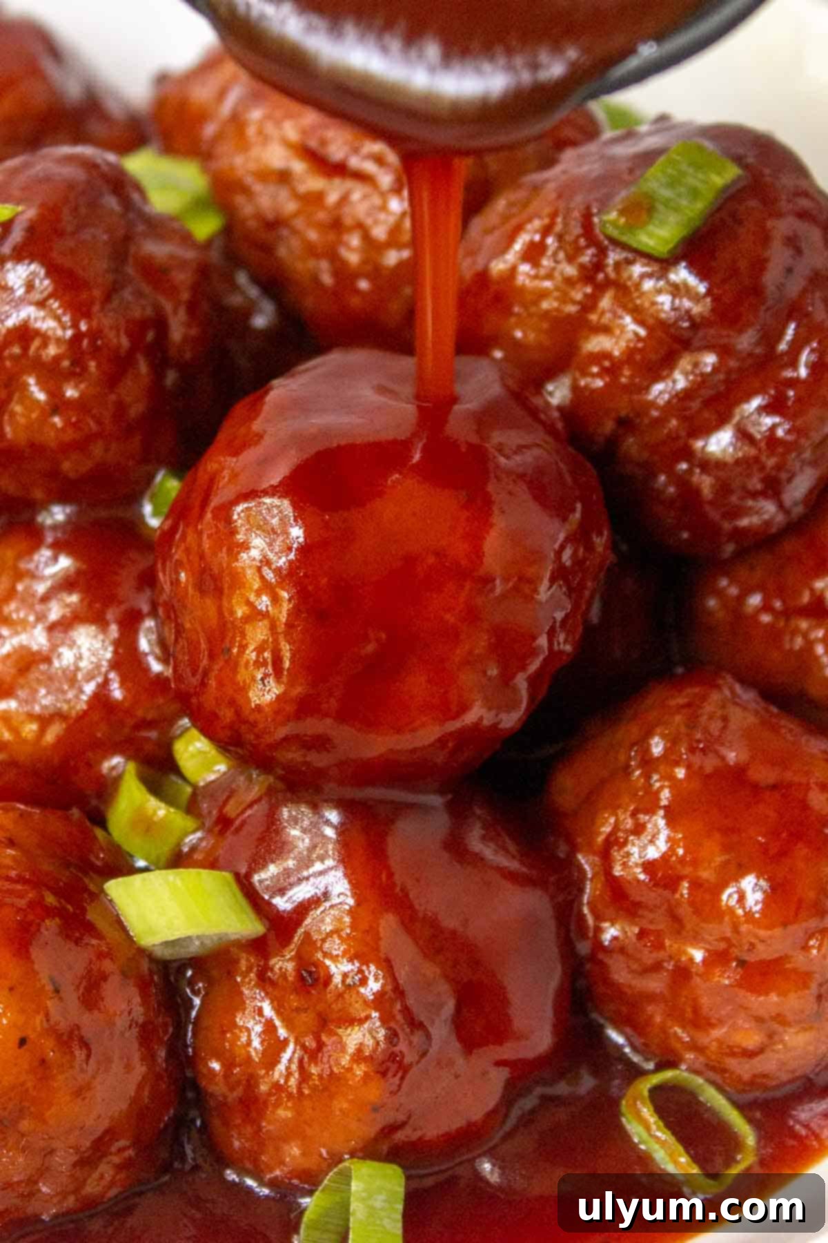 Grape jelly sauce being poured generously over a pile of Instant Pot Grape Jelly Meatballs in a serving bowl.