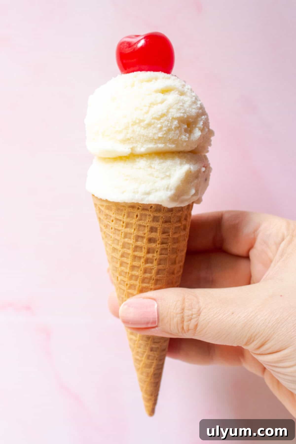 Two scoops of creamy Ninja Creami Vanilla Ice Cream on a sugar cone, topped with a maraschino cherry