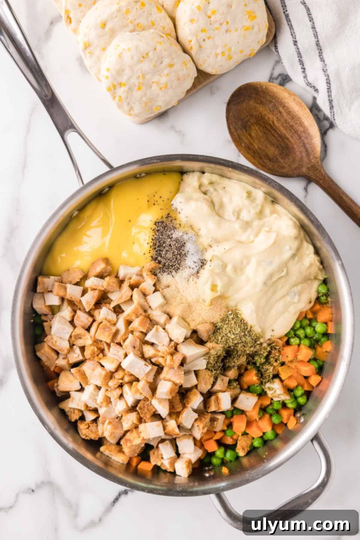 Chicken pot pie casserole filling ingredients added to a large skillet, showing butter and frozen vegetables