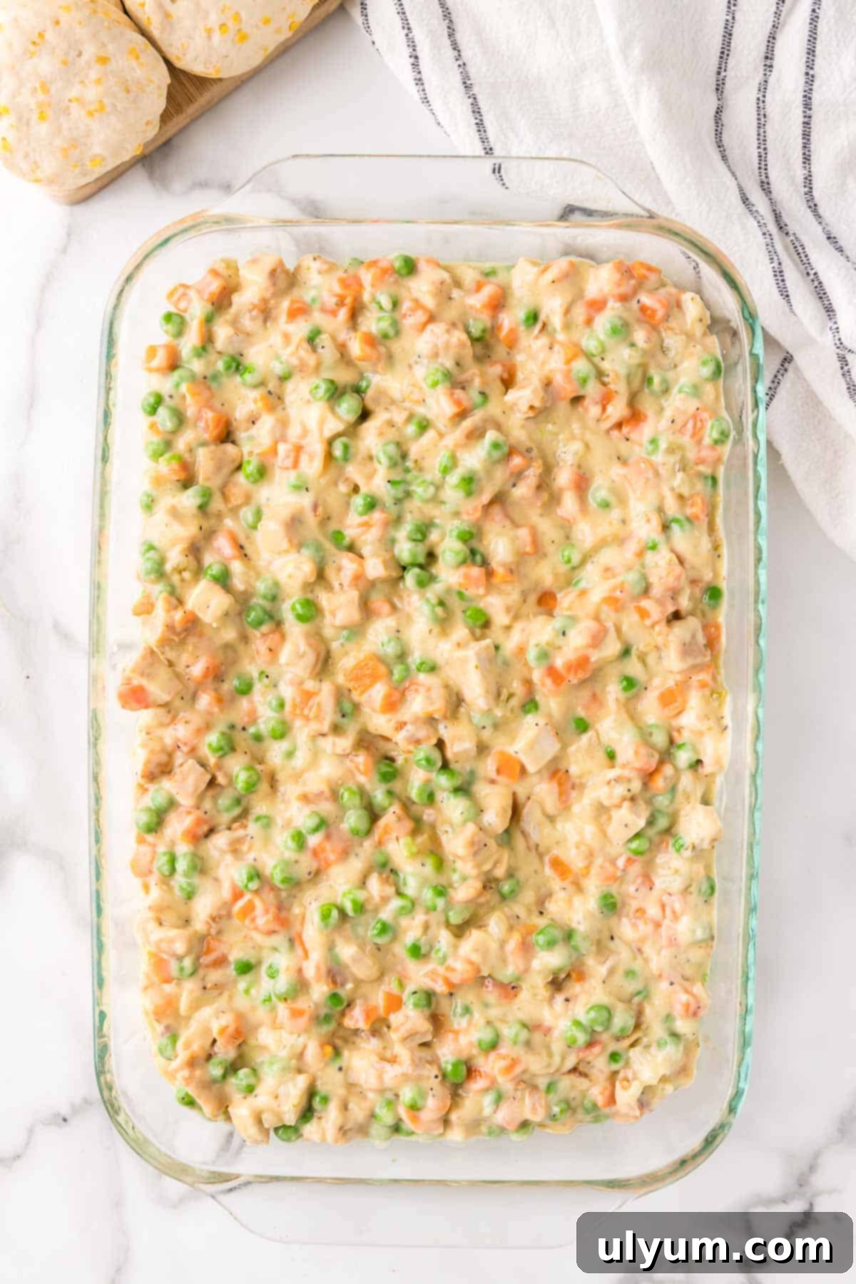 The chicken pot pie filling is spread evenly in a 9 by 13 inch baking dish, ready for biscuits