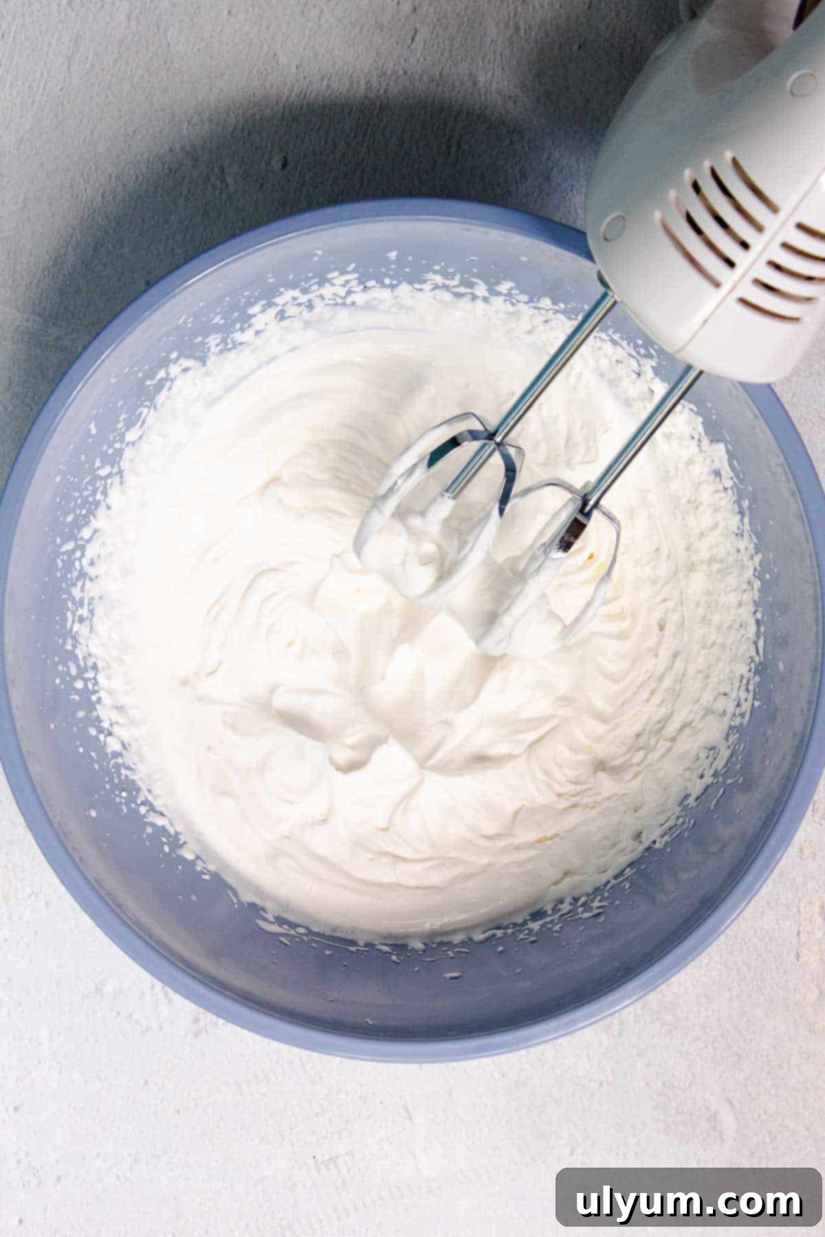 Remaining heavy cream has been whipped to stiff peaks using a hand mixer, forming fluffy whipped cream