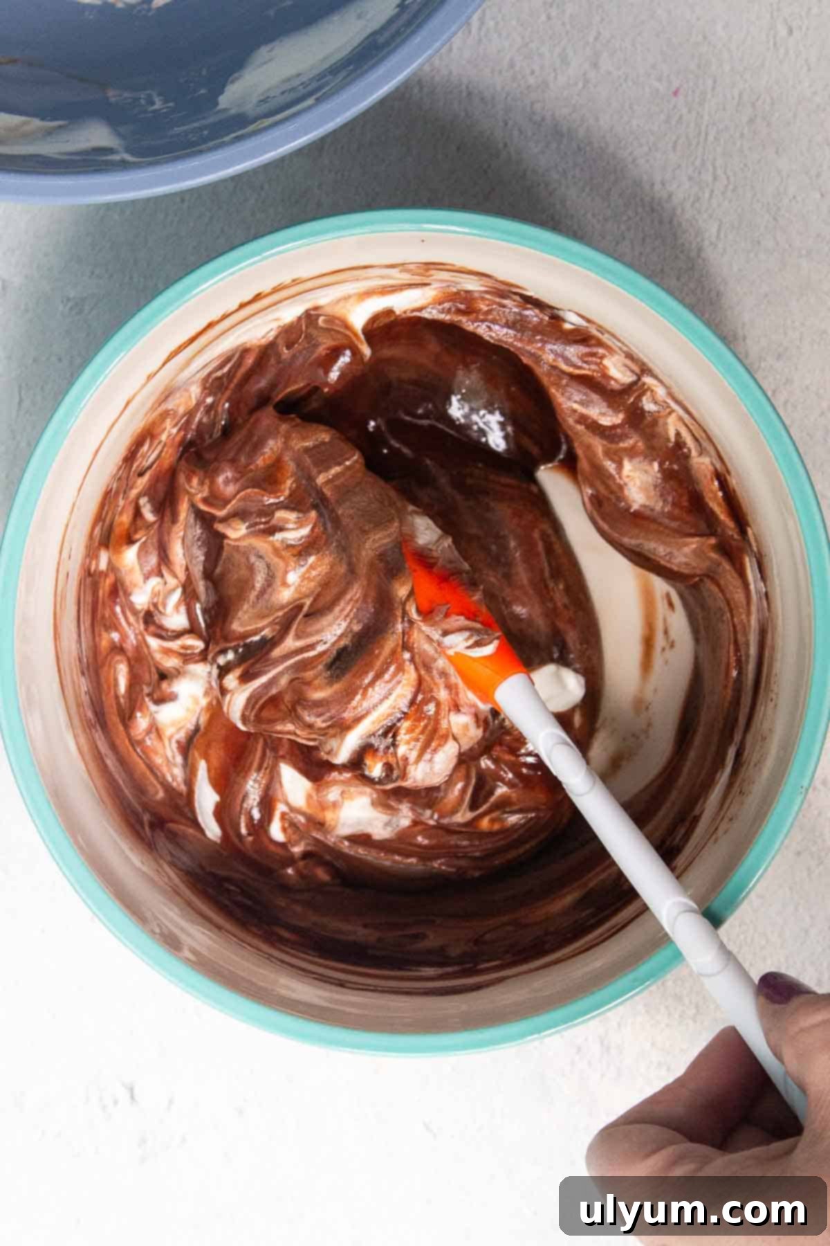 Whipped cream is being gently folded into the cooled chocolate mixture with a silicone spatula to maintain aeration
