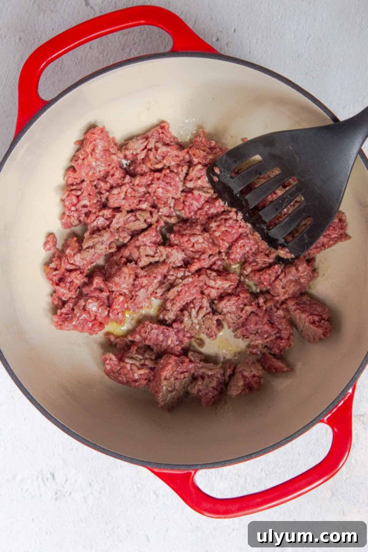 The ground beef is being browned in a large pot and is being broken up into smaller pieces with a spatula