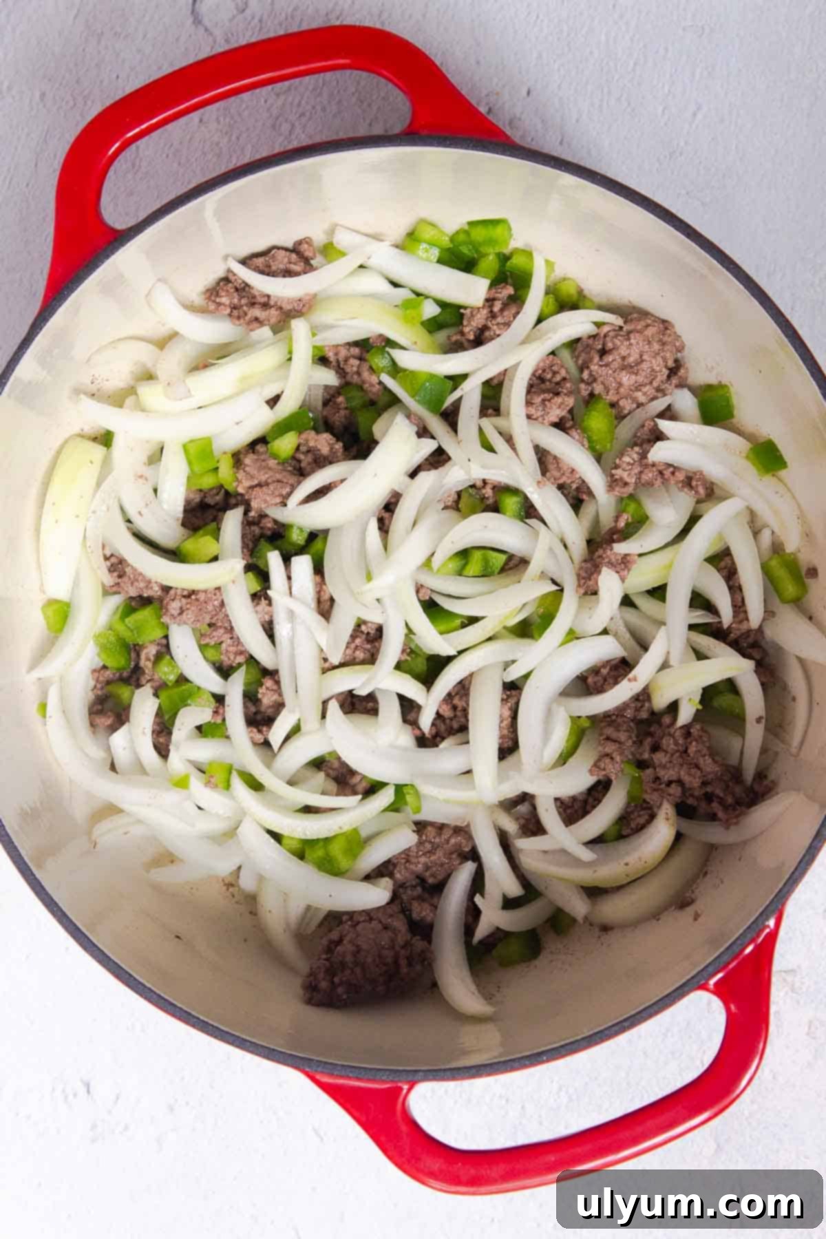 Sliced onions and diced green bell peppers are added to the browned beef