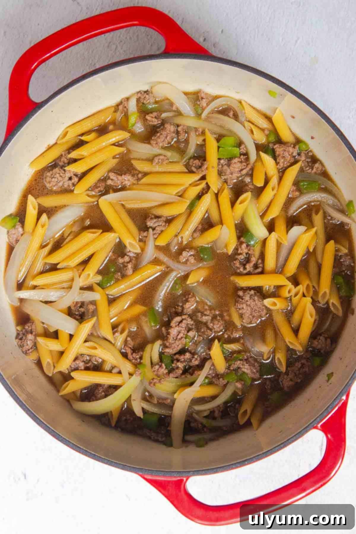 Uncooked pasta and beef broth are added to the meat mixture in the large pot