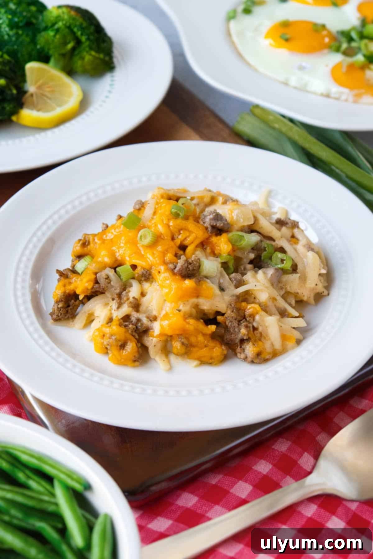 A golden-brown hash brown casserole served alongside vibrant green beans, fresh broccoli florets, and perfectly fried eggs with runny yolks, creating a balanced and inviting meal.