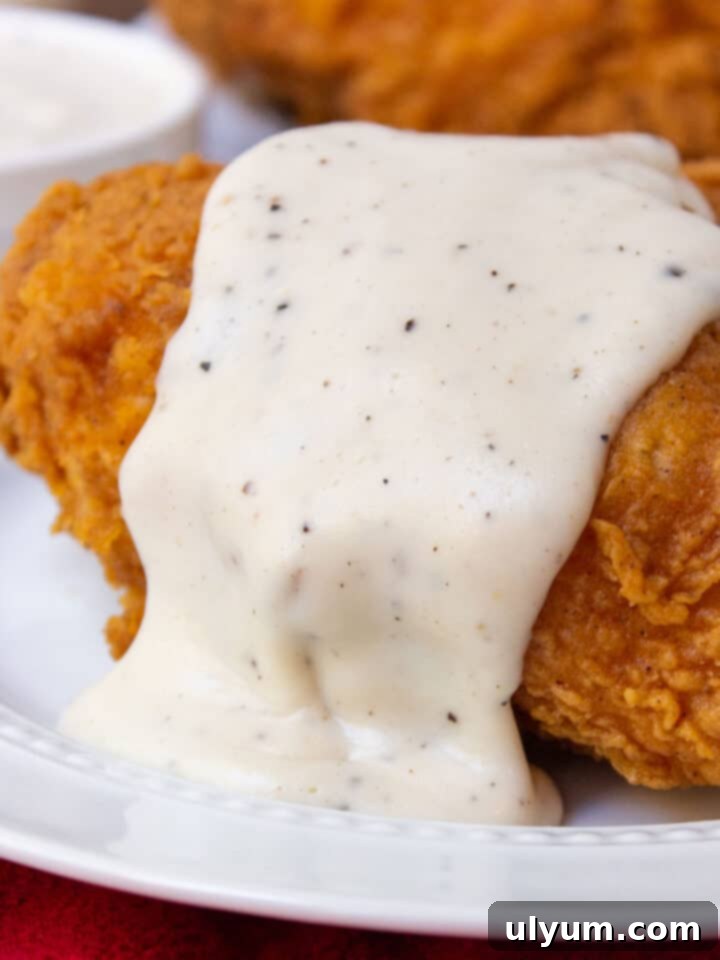 Rich Southern Country Gravy generously drizzled over crispy fried chicken, a creamy and savory Southern staple.