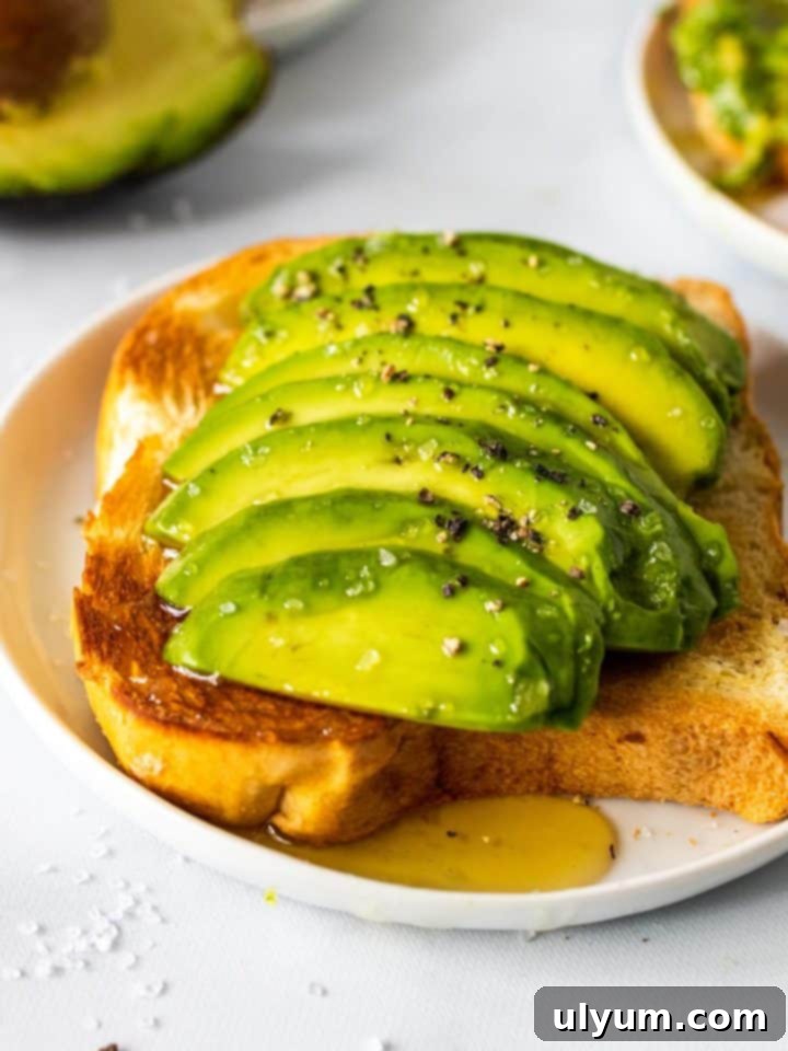 A slice of golden toast topped with thick slices of creamy avocado, seasoned with sea salt and coarse black pepper, and finished with a sweet drizzle of honey.