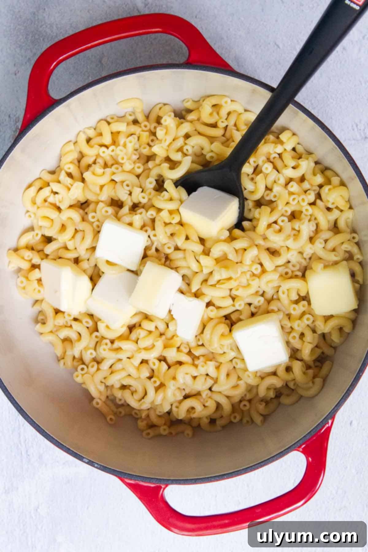 Slices of butter melting into cooked elbow macaroni noodles in a large pot.