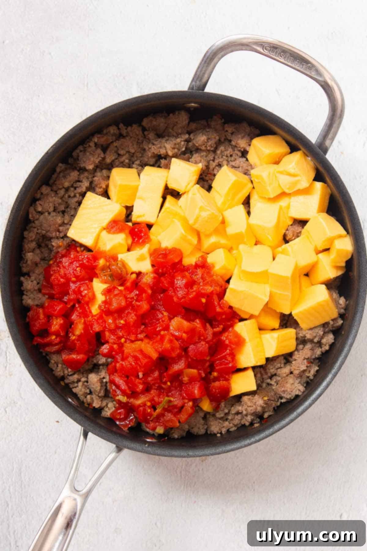 Ultimate Velveeta Sausage Dip 5 Cubed Velveeta cheese and an undrained can of Rotel diced tomatoes and green chilies are added to the browned sausage in a large skillet, ready for melting.