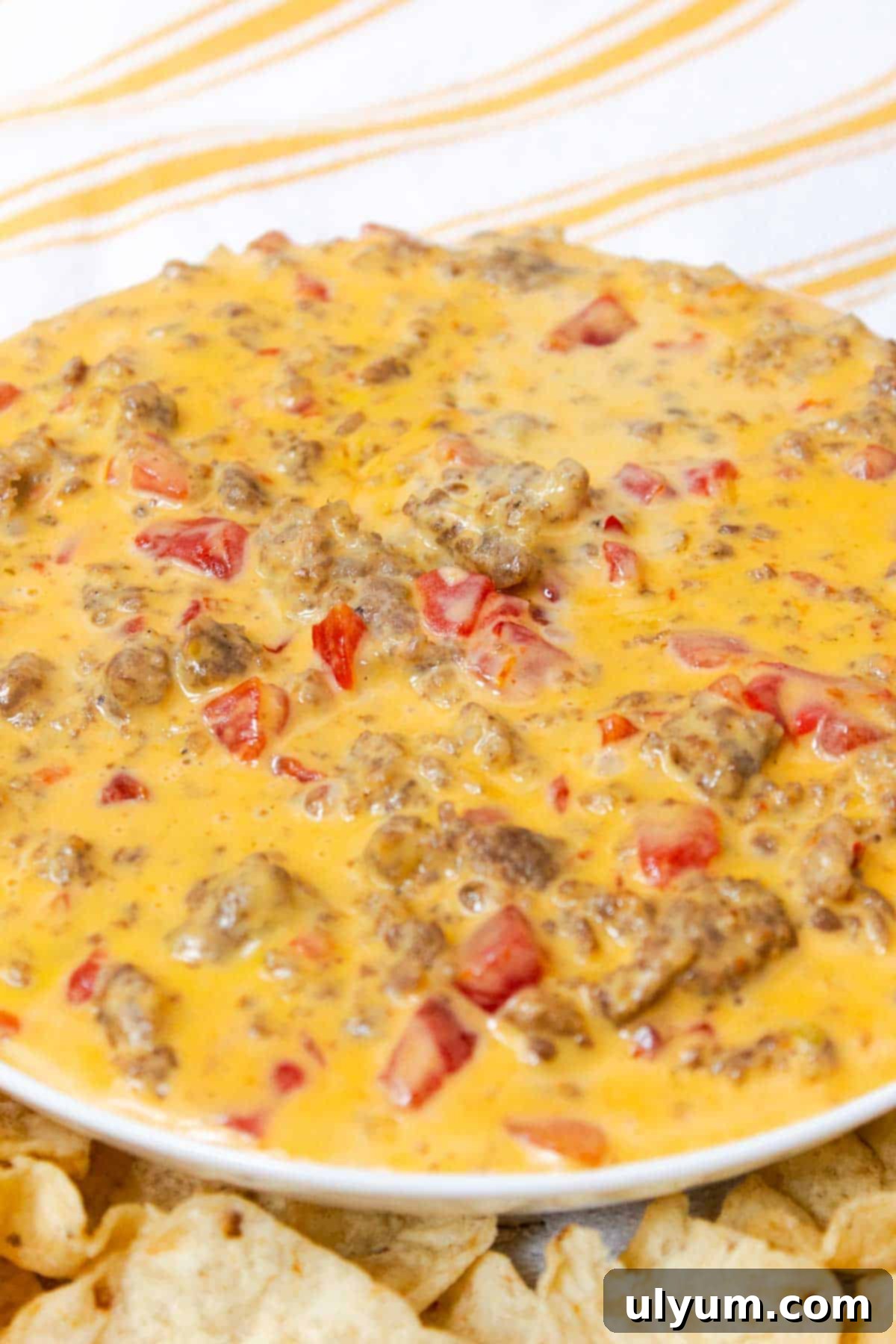 Ultimate Velveeta Sausage Dip 7 A vibrant bowl of Velveeta Sausage Cheese Dip, garnished with fresh cilantro, surrounded by a colorful assortment of tortilla chips, red bell peppers, and carrot sticks.