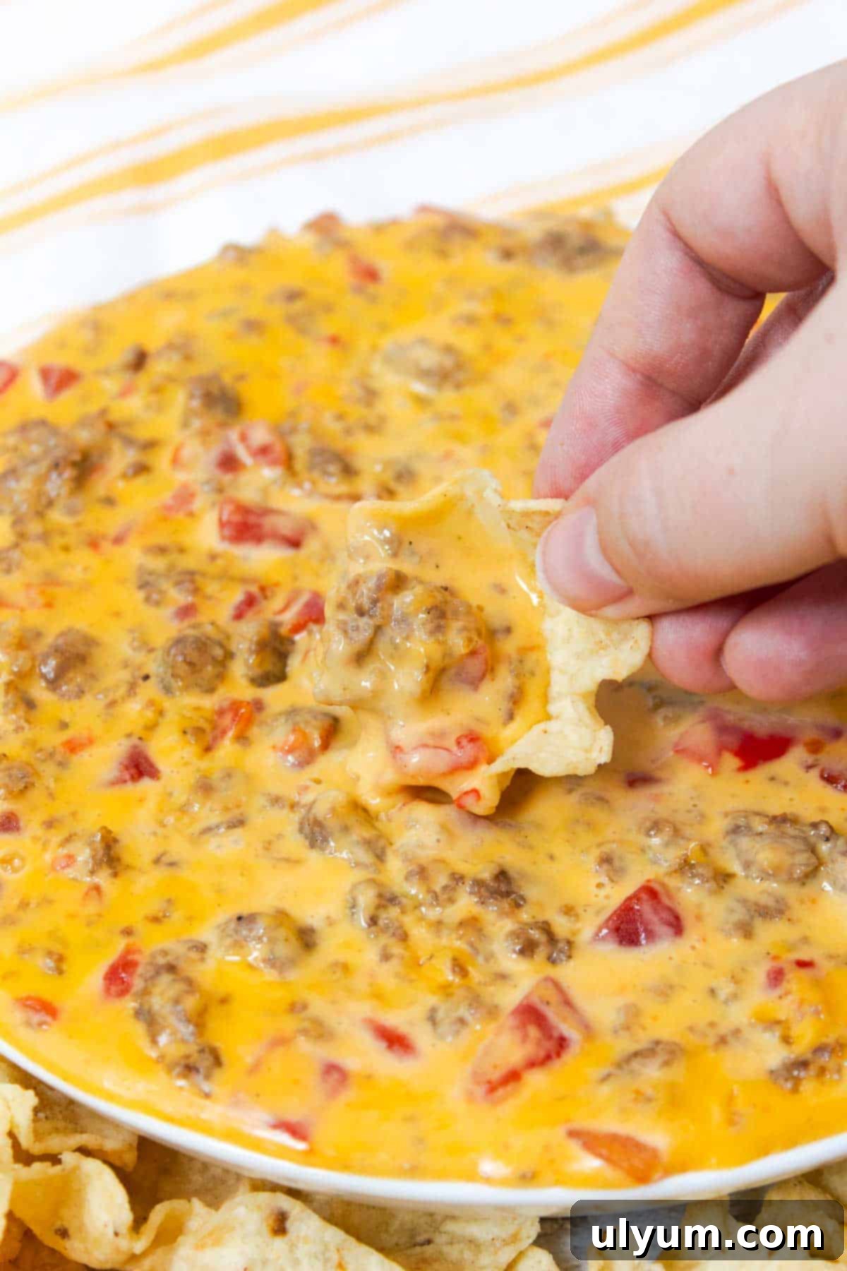 Ultimate Velveeta Sausage Dip 8 A scoop-style tortilla chip laden with a generous amount of Velveeta Sausage Cheese Dip, showcasing its creamy texture and bits of sausage and tomato.