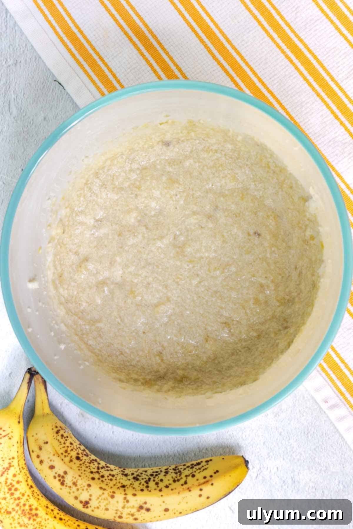 A bowl containing the combined wet ingredients for the banana coffee cake batter, including mashed banana, egg, sour cream, and vanilla extract, mixed until smooth.