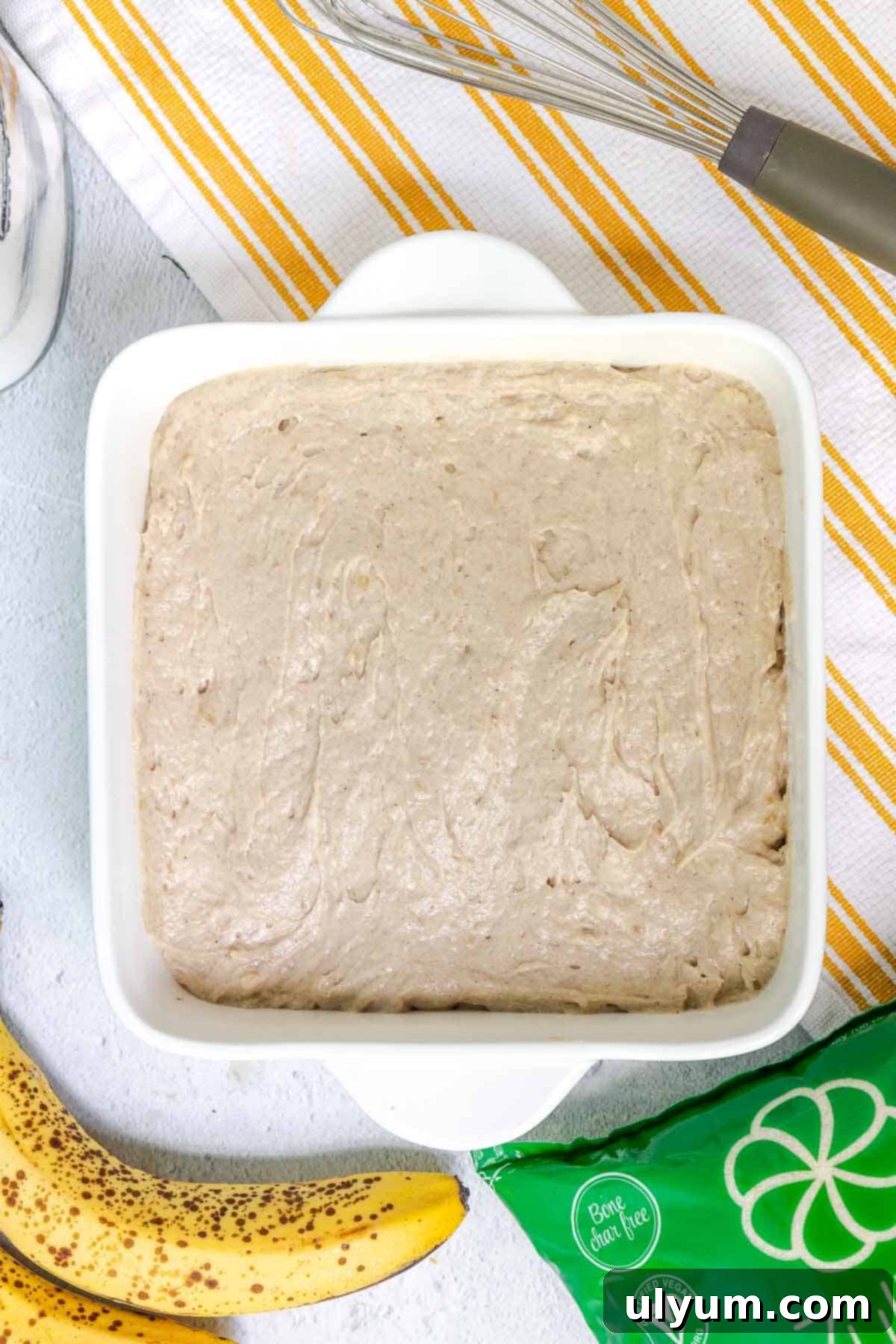 Banana cake batter spread evenly in an 8x8 baking dish, ready for the crumble topping.