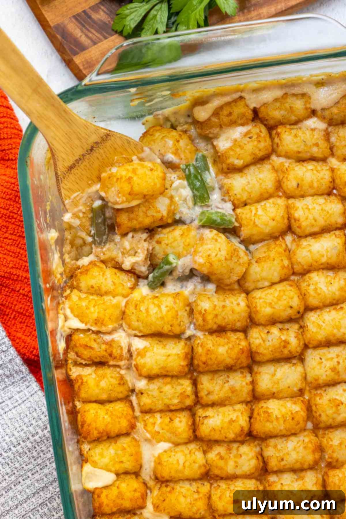 A scoop is taken out of the casserole dish to show the creamy inside of the casserole, featuring ground beef, green beans, and melted cheese.