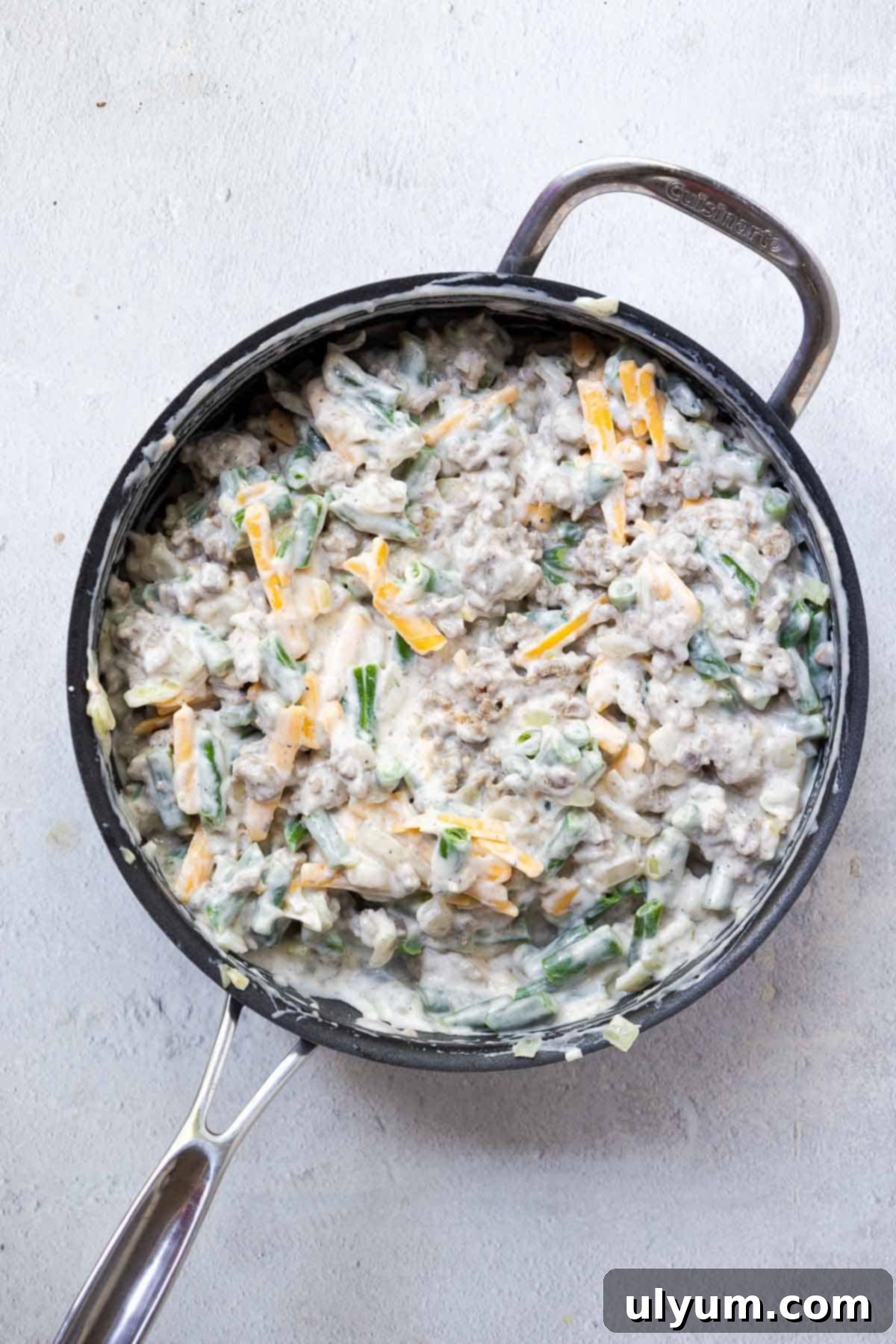 The soup, sour cream, milk, green beans, cheese, and seasonings are mixed together in the skillet with the beef and onions, creating a creamy base.