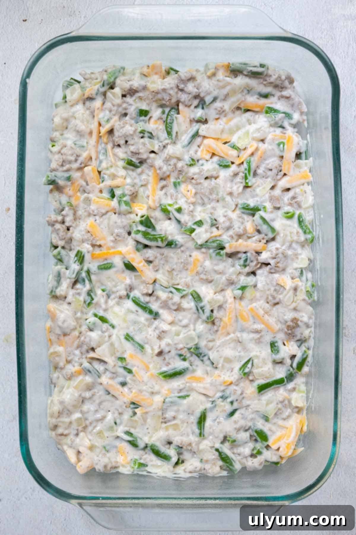 The green bean and meat mixture is spread evenly in the bottom of a 9 by 13 inch casserole dish, forming the flavorful base.