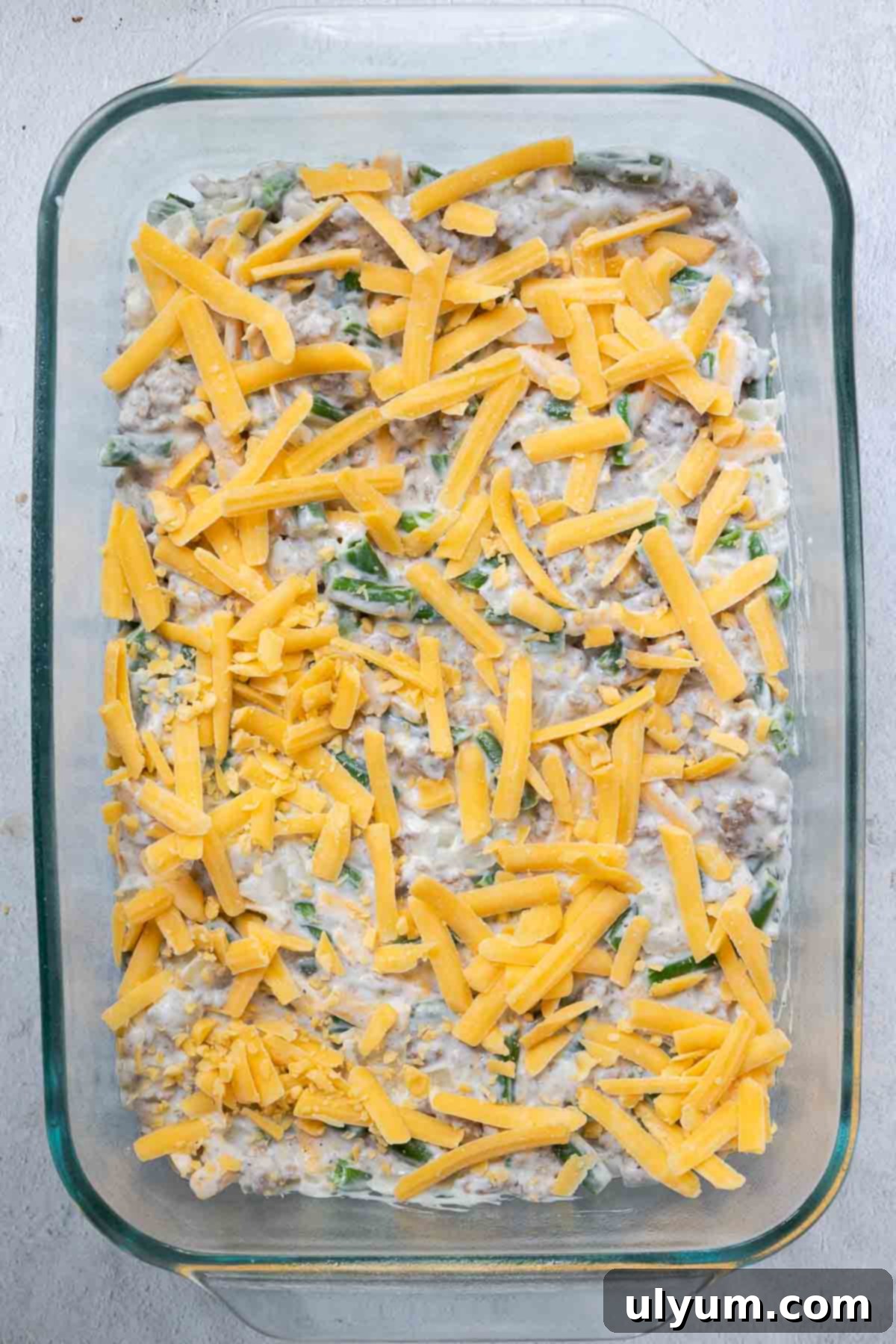 Shredded cheddar cheese is sprinkled evenly over the meat mixture, adding a layer of cheesy goodness.