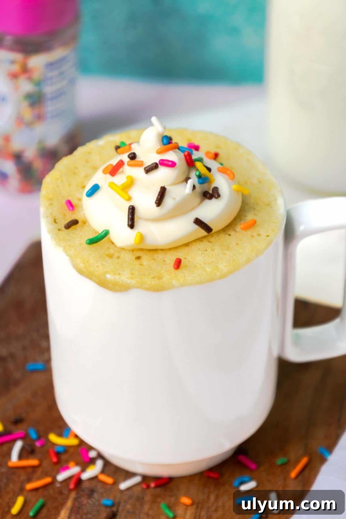 Yellow mug cake topped with buttercream frosting and sprinkles.