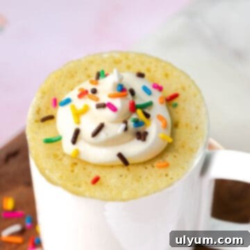 Yellow mug cake topped with buttercream frosting and sprinkles.