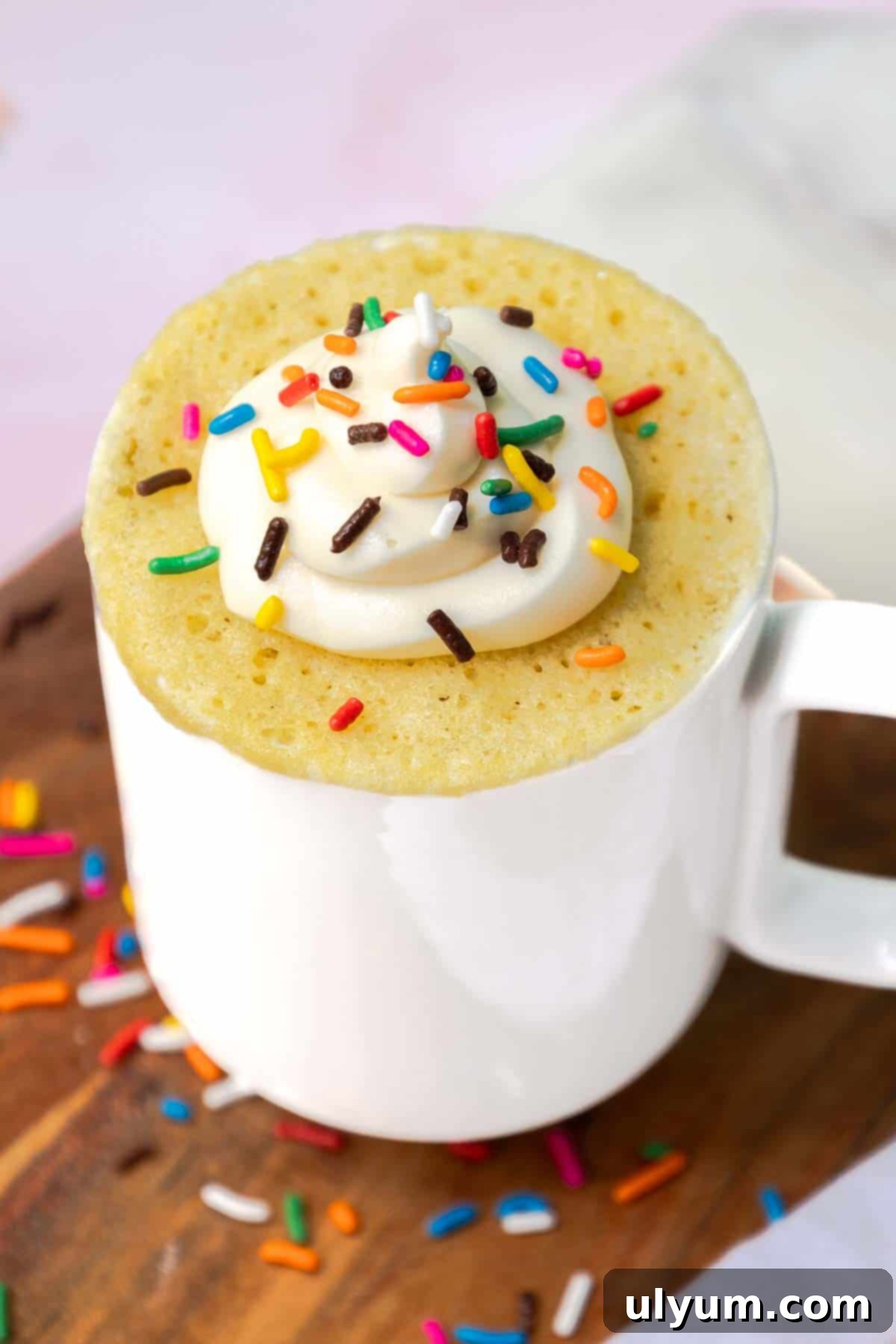 Yellow mug cake topped with buttercream frosting and sprinkles