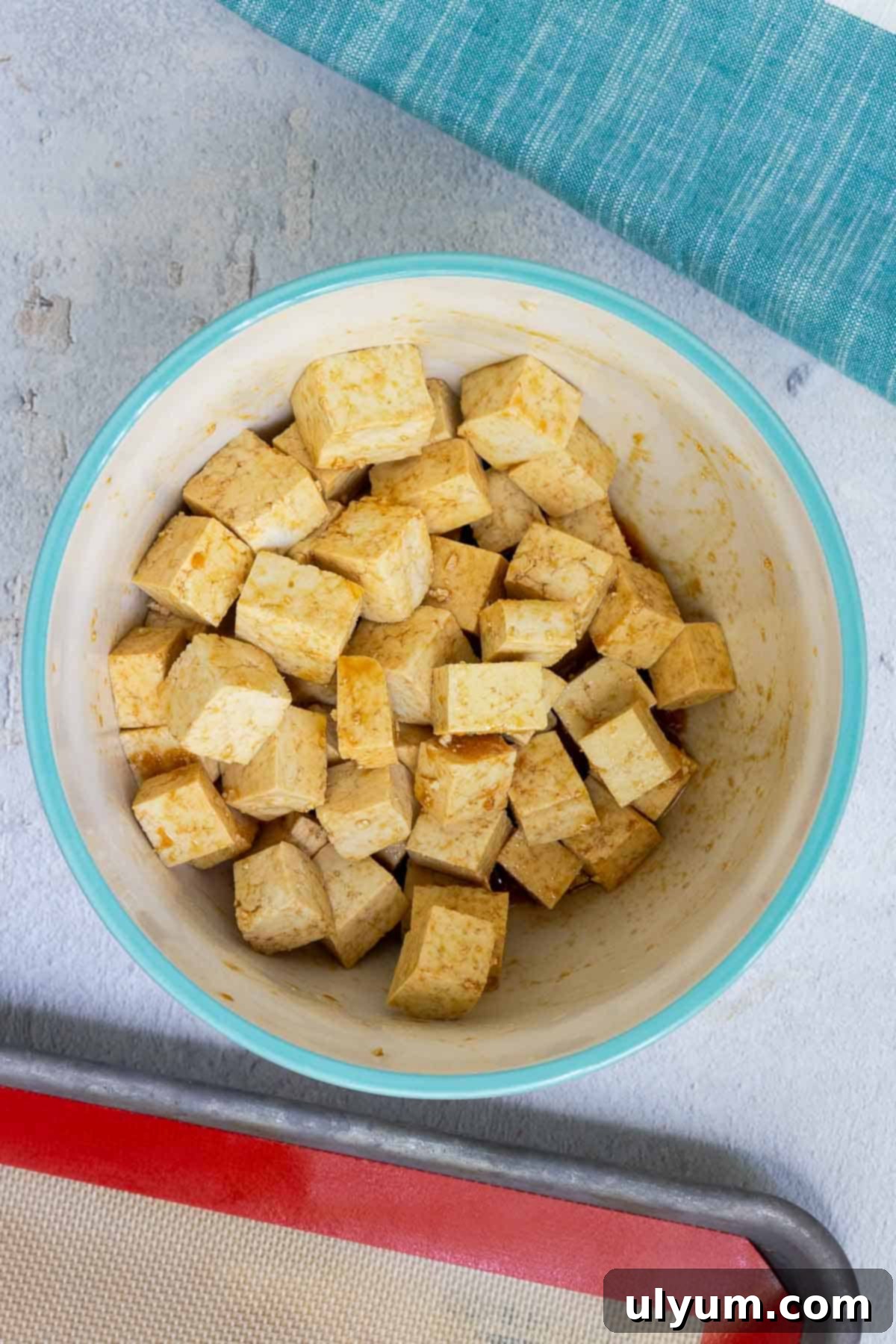 Cubed tofu is thoroughly tossed in a savory soy sauce marinade, ensuring each piece is well-coated.