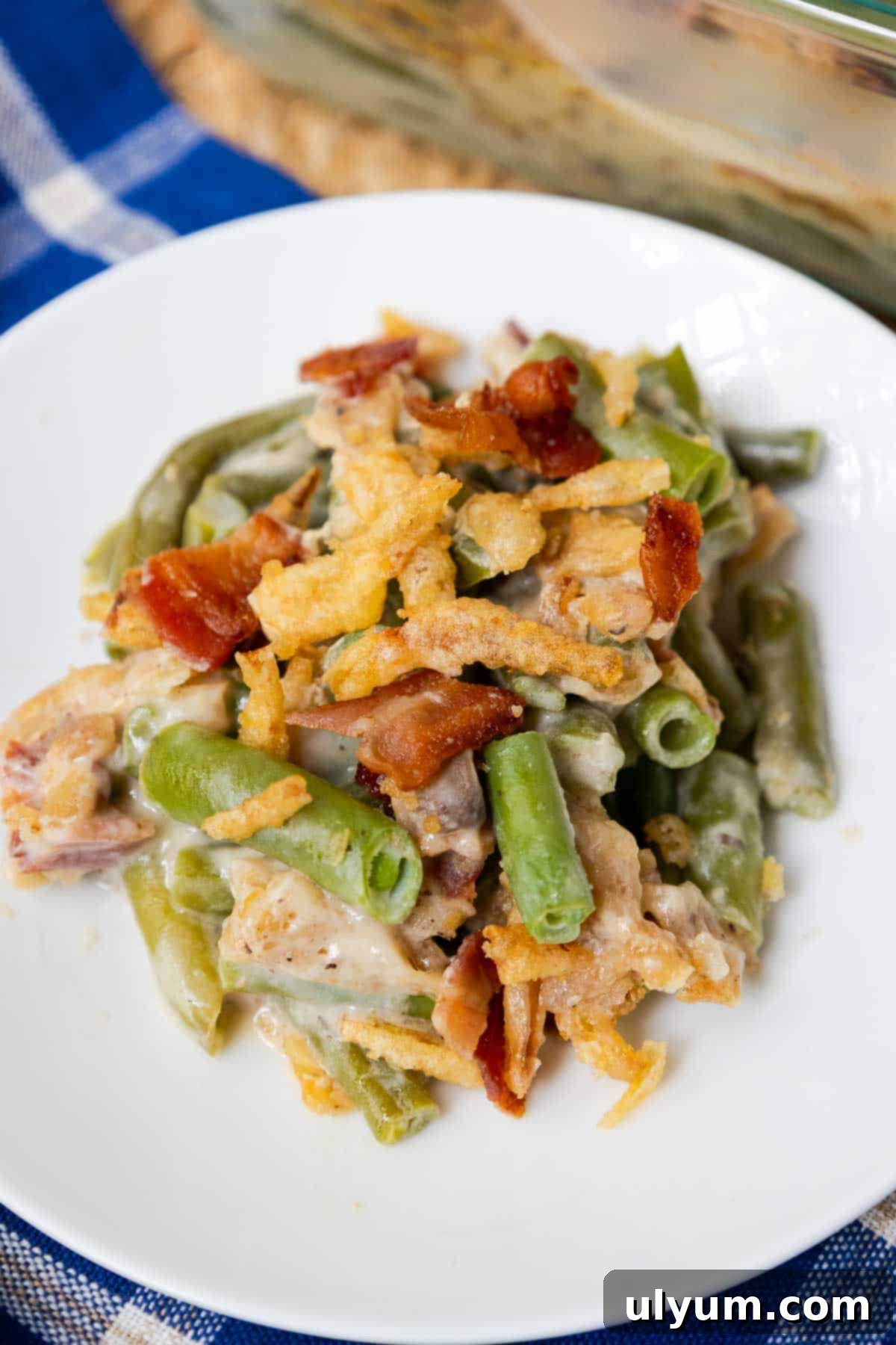 Side of green bean casserole with bacon and crispy fried onions served on a plate.