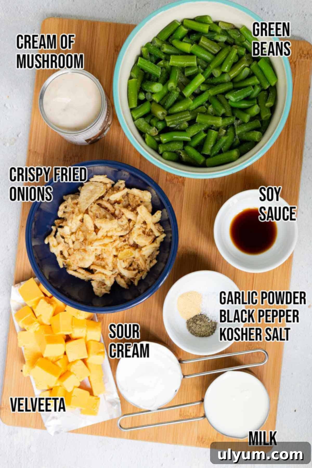 Ingredients laid out for Velveeta green bean casserole including cream of mushroom soup, milk, Velveeta, green beans, crispy fried onions, sour cream, soy sauce, garlic powder, black pepper, and salt.