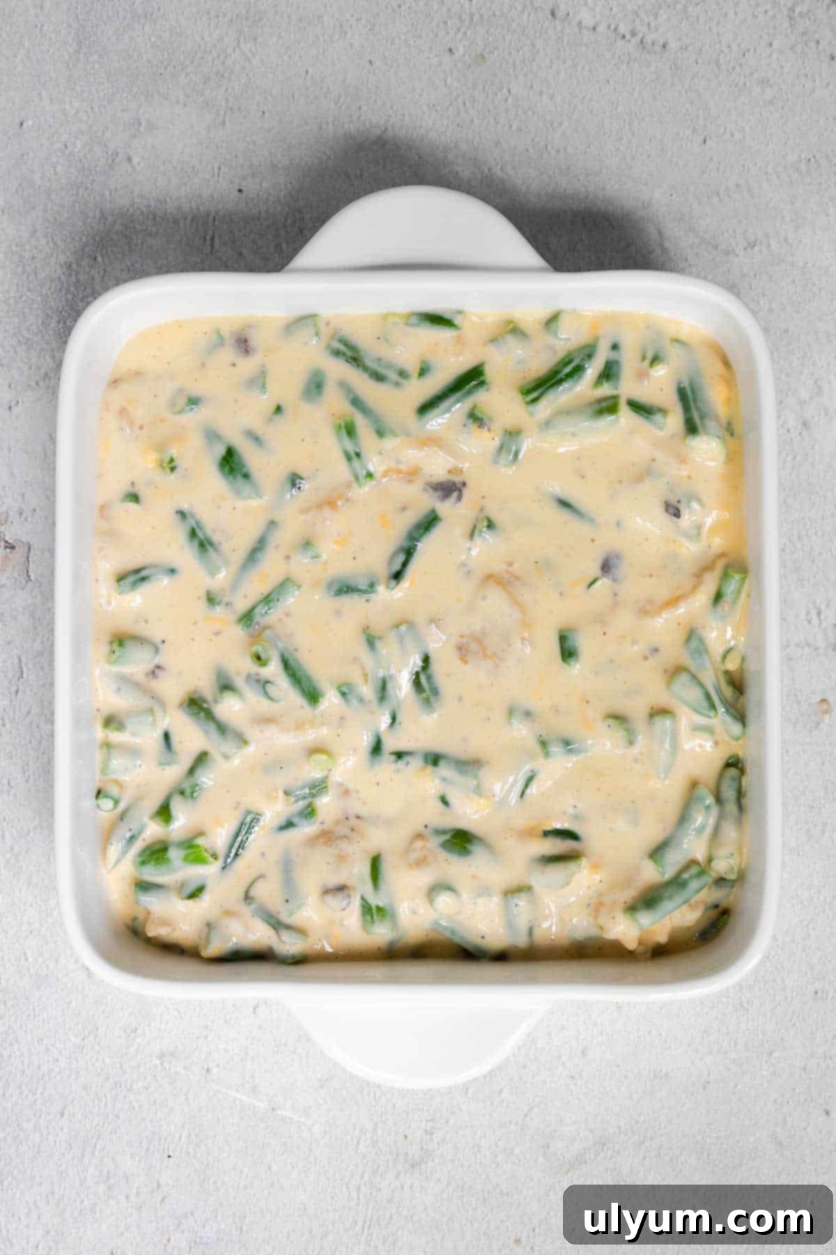 The mixed green bean casserole filling spread evenly in an 8x8 inch baking dish.