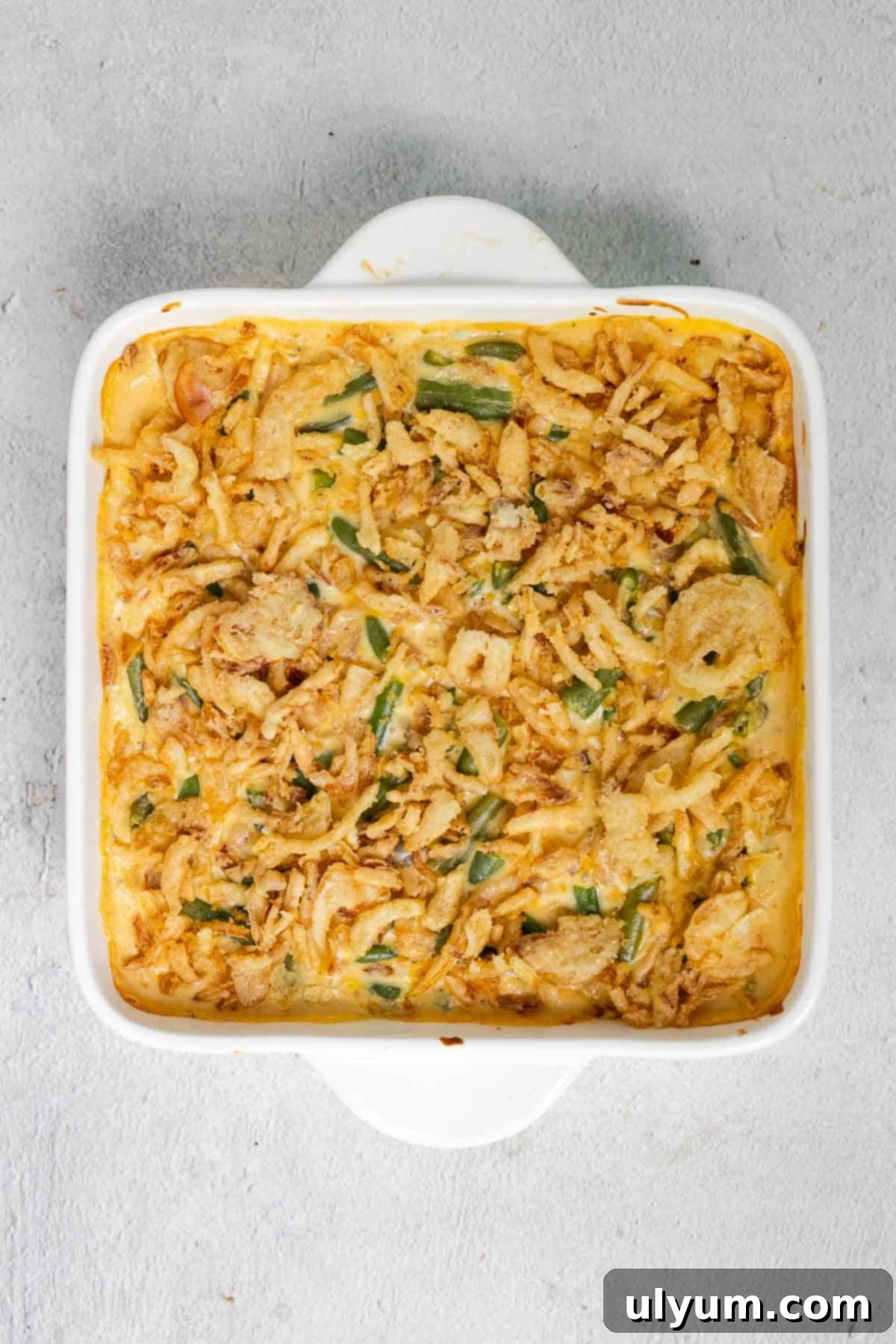 Crispy fried onions being added to the top of the warm Velveeta green bean casserole.