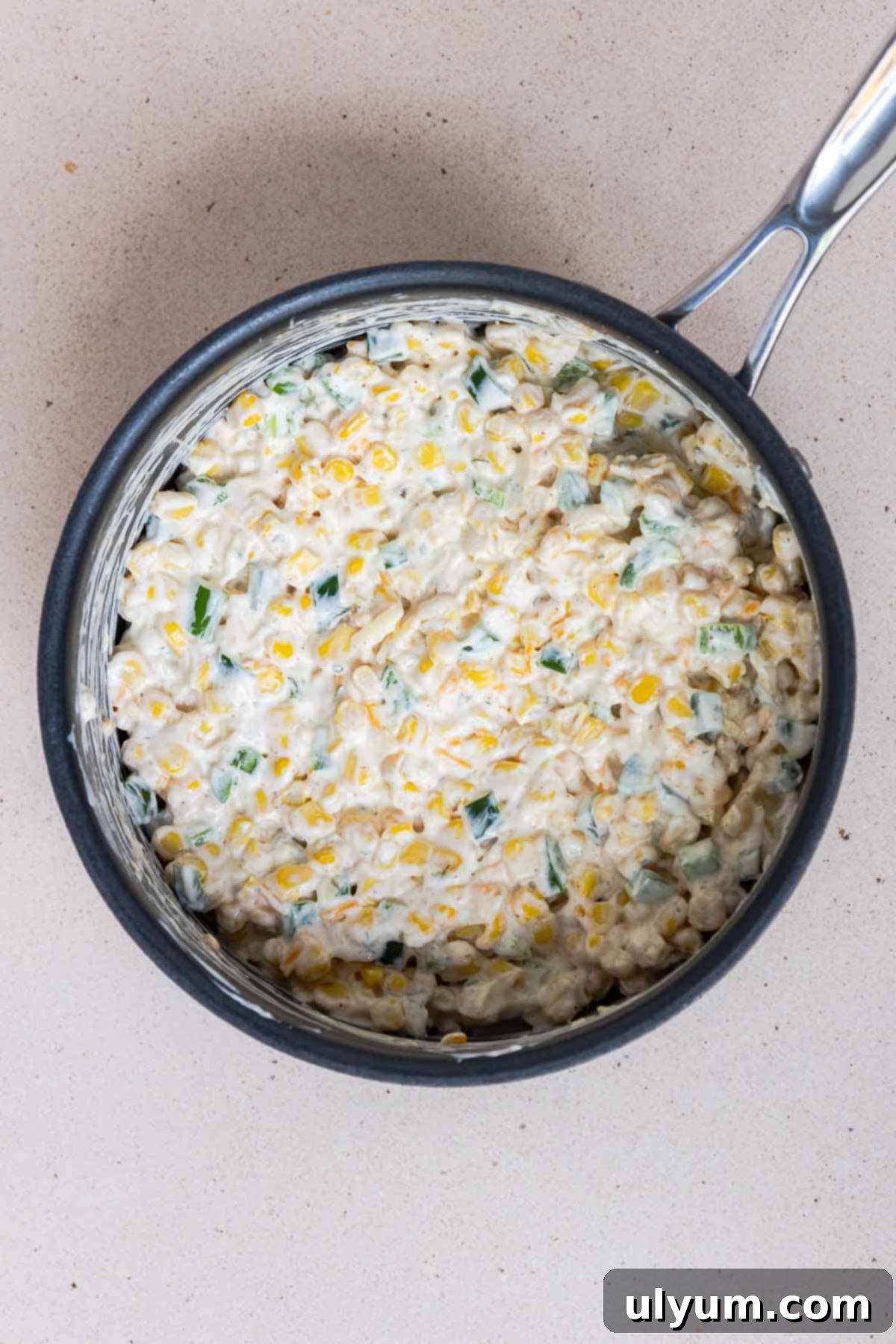 The corn casserole ingredients are coated evenly in the cream cheese mixture in the saucepan.