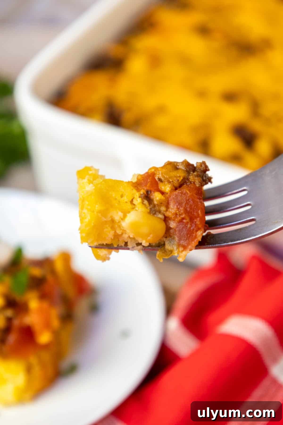 A fork taking a bite of Mexican cornbread casserole, clearly showing the distinct layers of fluffy cornbread and seasoned beef.