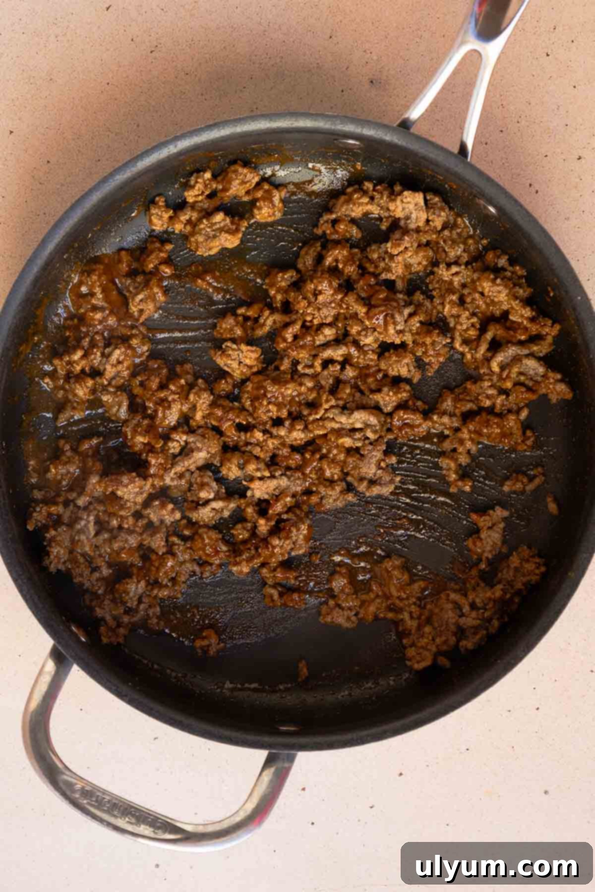 Ground beef cooking in a large skillet, simmering with taco seasoning and water until the liquid thickens, creating a flavorful meat base for the casserole.
