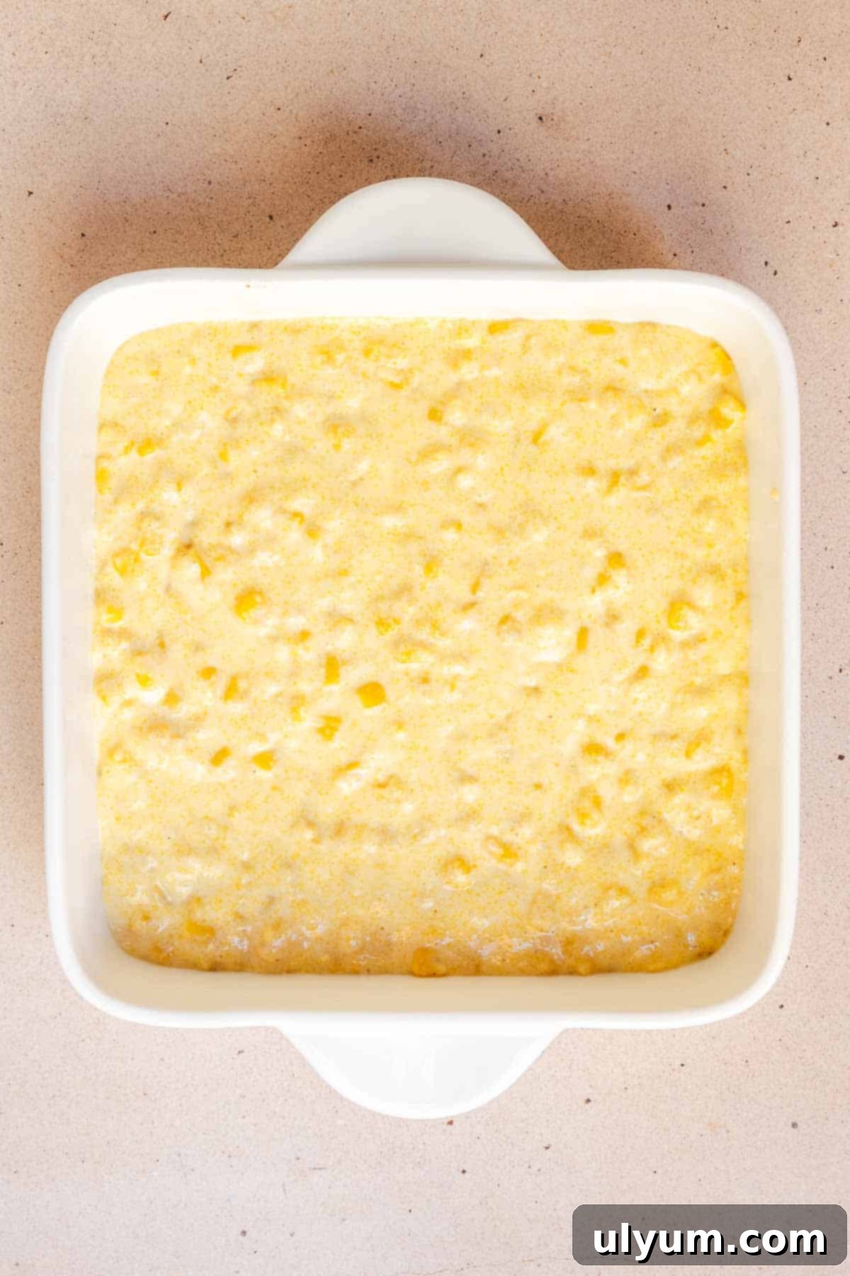 The prepared cornbread mixture is spread evenly across the bottom of an 8x8 inch baking dish, ready for the next layer.