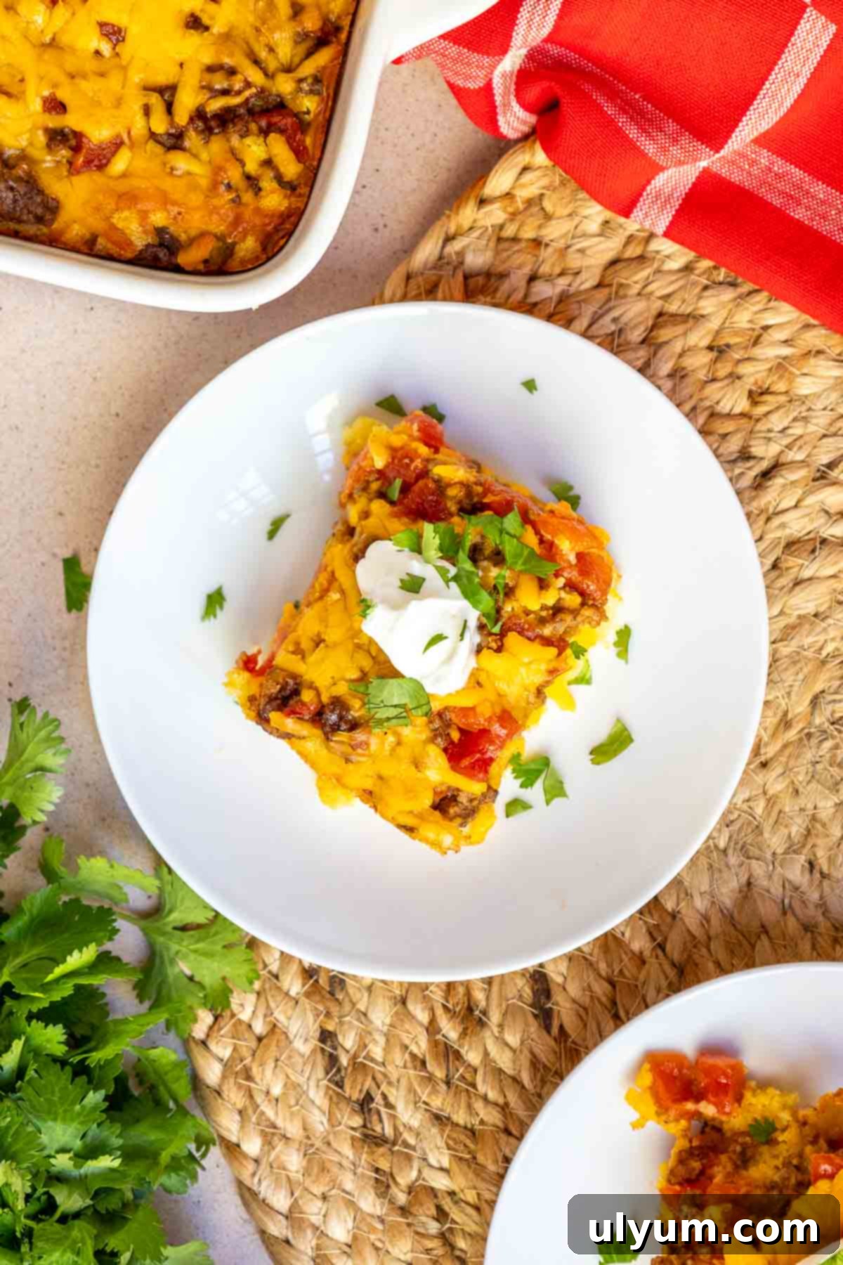 A single serving of Mexican cornbread casserole beautifully plated, generously garnished with a dollop of sour cream and a sprinkle of fresh chopped cilantro.