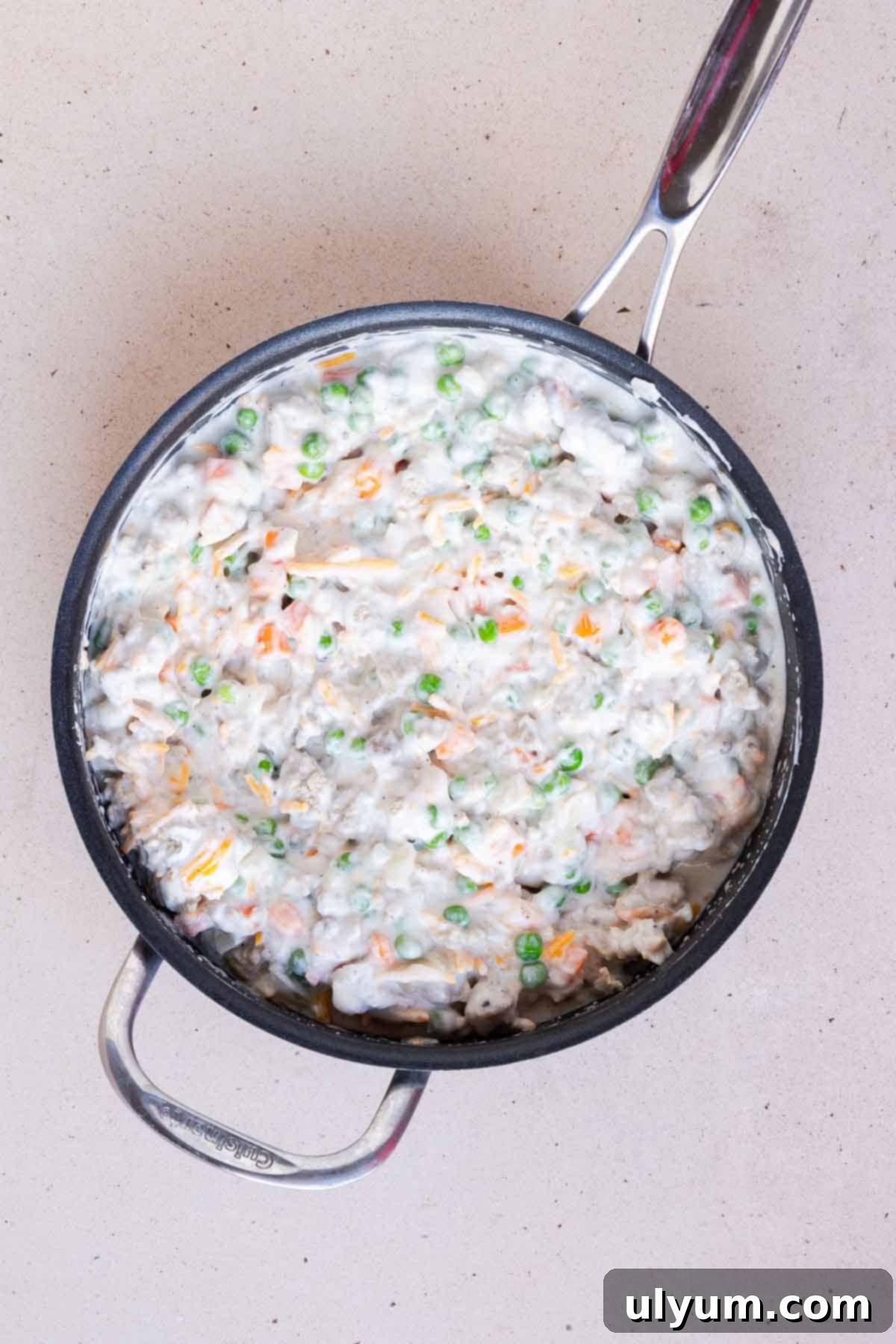 The soup, Greek yogurt, cheese, milk, and frozen peas and carrots are mixed together with the turkey and onion mixture in the large skillet.