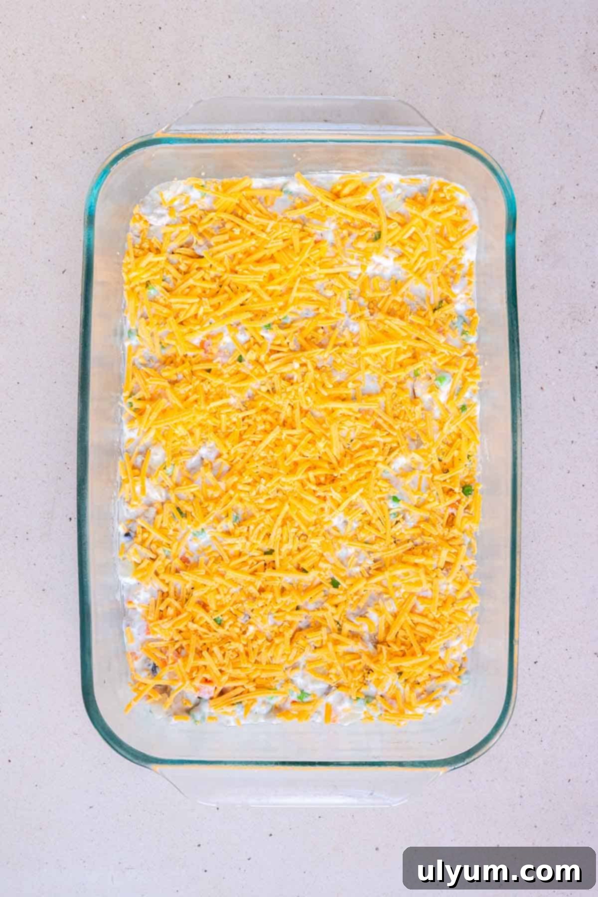 The casserole filling is topped with an even layer of shredded cheddar.