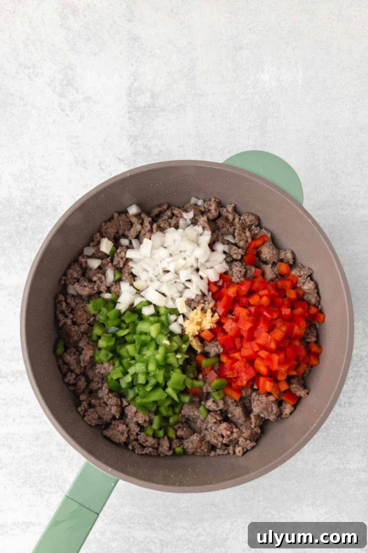 Diced onion, garlic, and bell peppers are added to the sausage in the skillet.