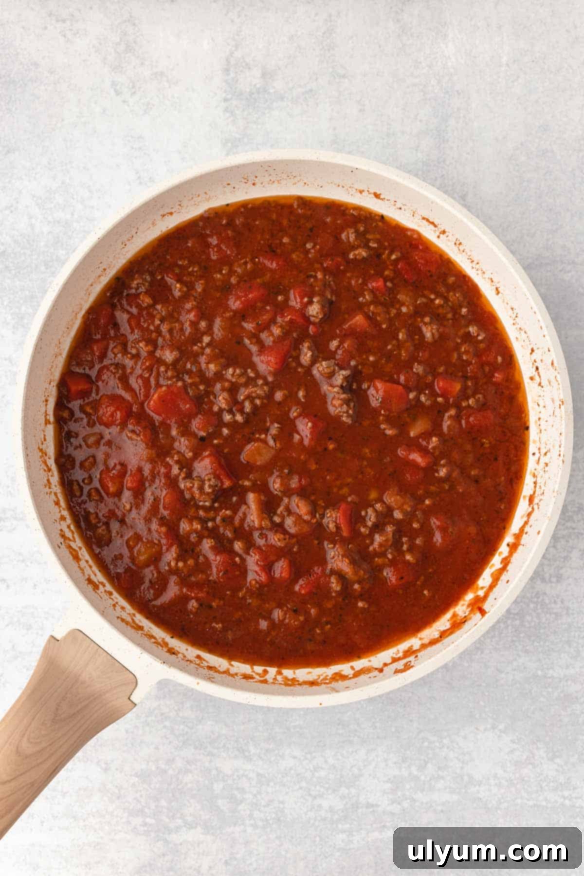 The meat sauce for the ground beef noodle casserole is simmering in a large skillet.