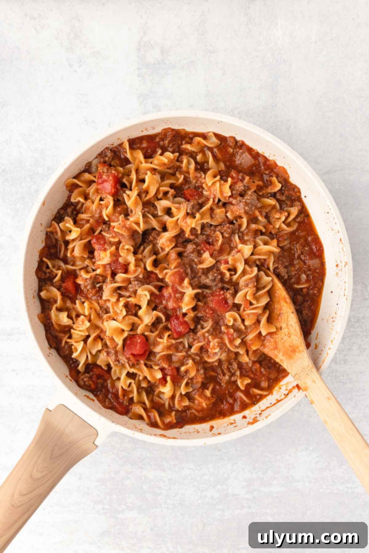 The cooked egg noodles are added back to the skillet and combined with the meat sauce for the casserole.