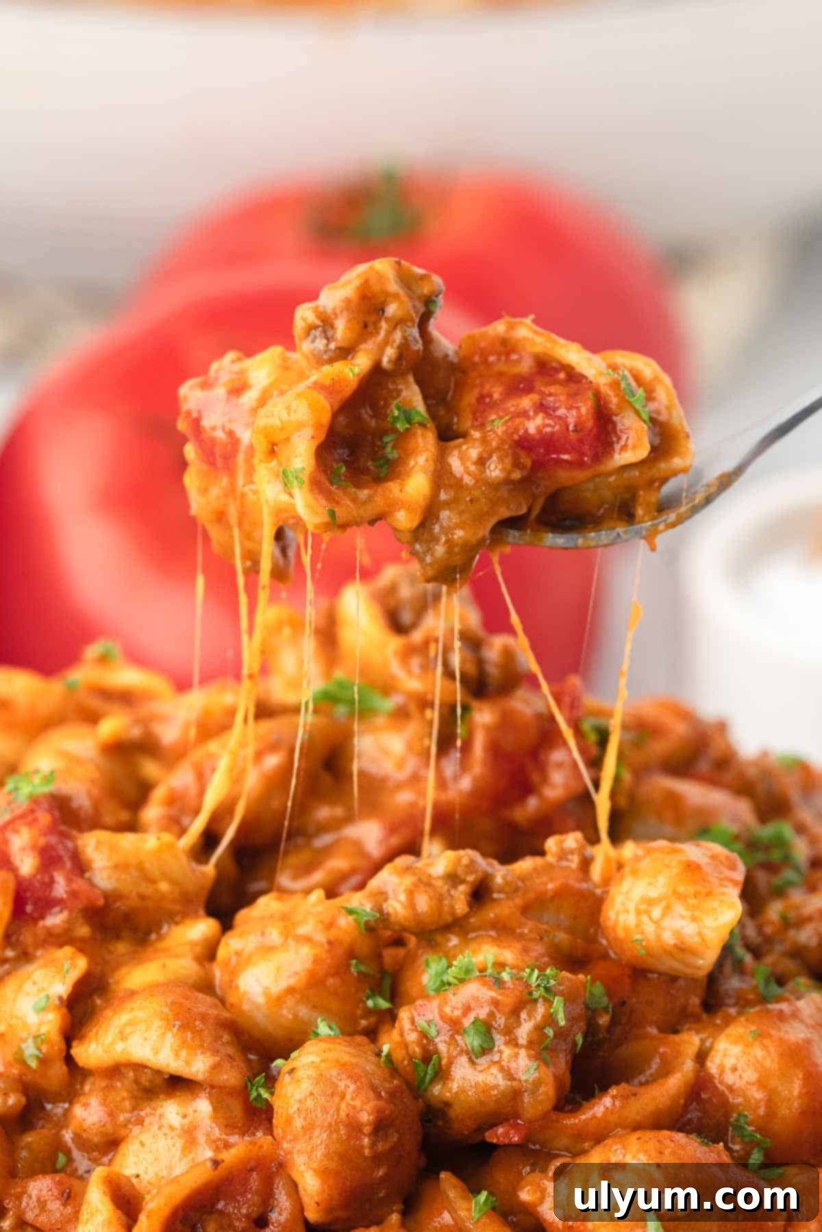 The Ultimate One-Pot Cheesy Taco Pasta 13 A fork is scooping up a bite of taco pasta showing strings of cheese stretch from the fork to the bowl below.
