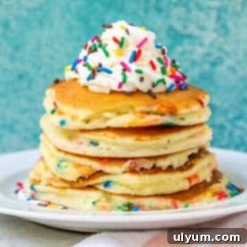 Stack of fluffy Funfetti pancakes topped with whipped cream and rainbow sprinkles, ready for a festive breakfast.