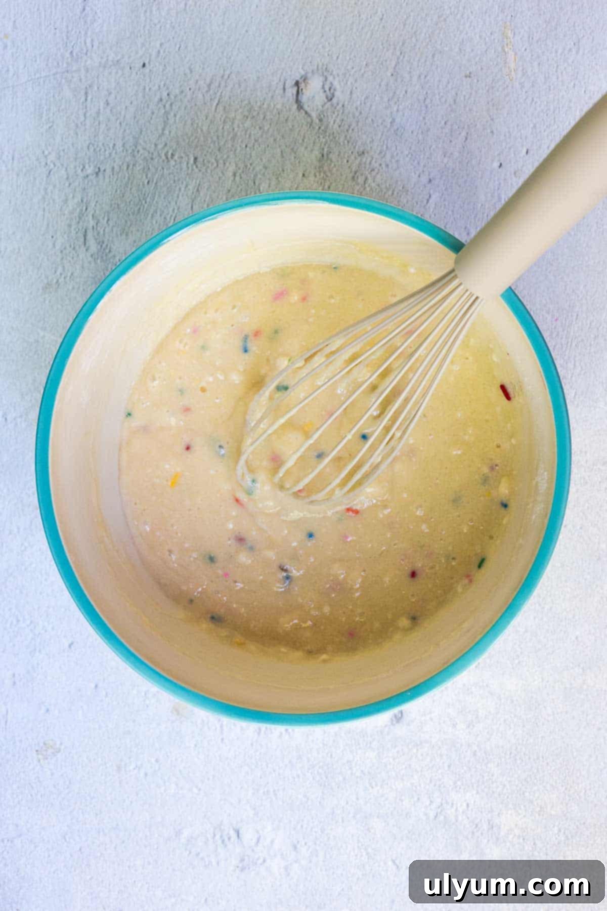 Funfetti pancake batter being mixed in a large bowl with a whisk until just combined.